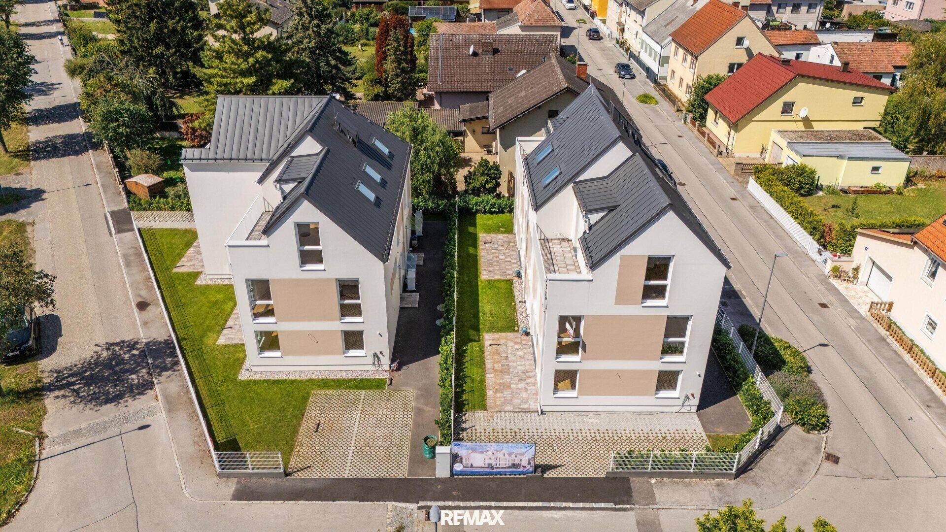 Luftaufnahme von zwei modernen Einfamilienhäusern mit Grundstücken, Zufahrten und Umgebung.