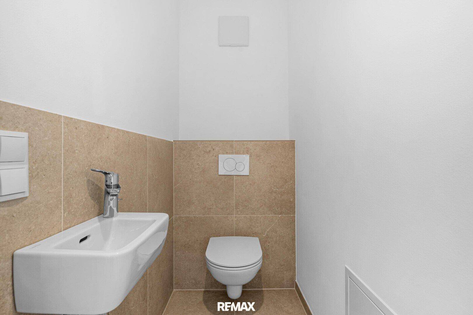 Funktionelles Gäste-WC mit wandhängendem WC, kleinem Waschbecken und beigefarbenen Fliesen.