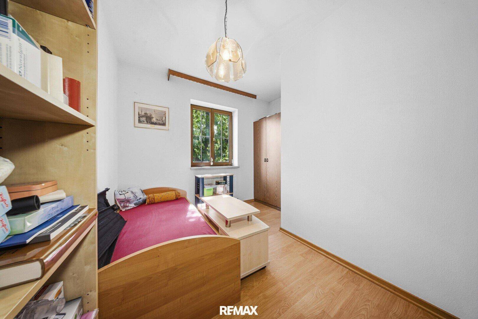 Kleines Schlafzimmer mit Holzboden, Fenster und einfacher Einrichtung.