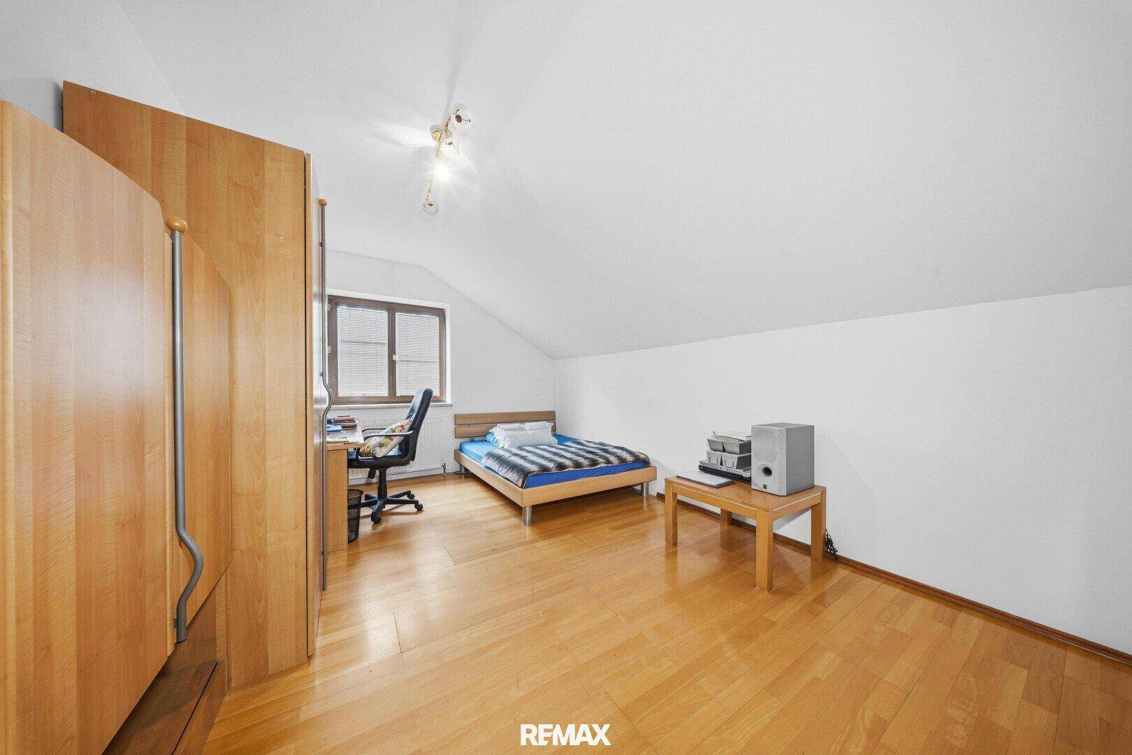 Schlafzimmer im Dachgeschoss mit Bett, Schreibtisch und Laminatboden.