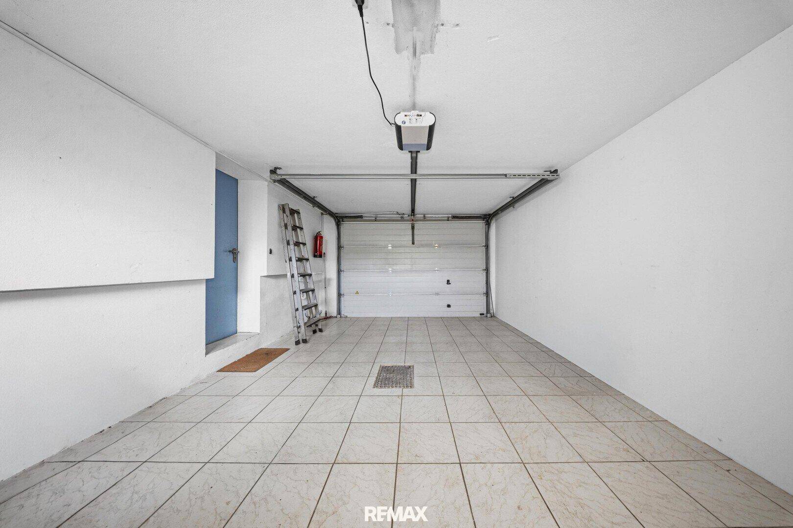 Geräumige Garage mit Fliesenboden und automatischem Garagentor.
