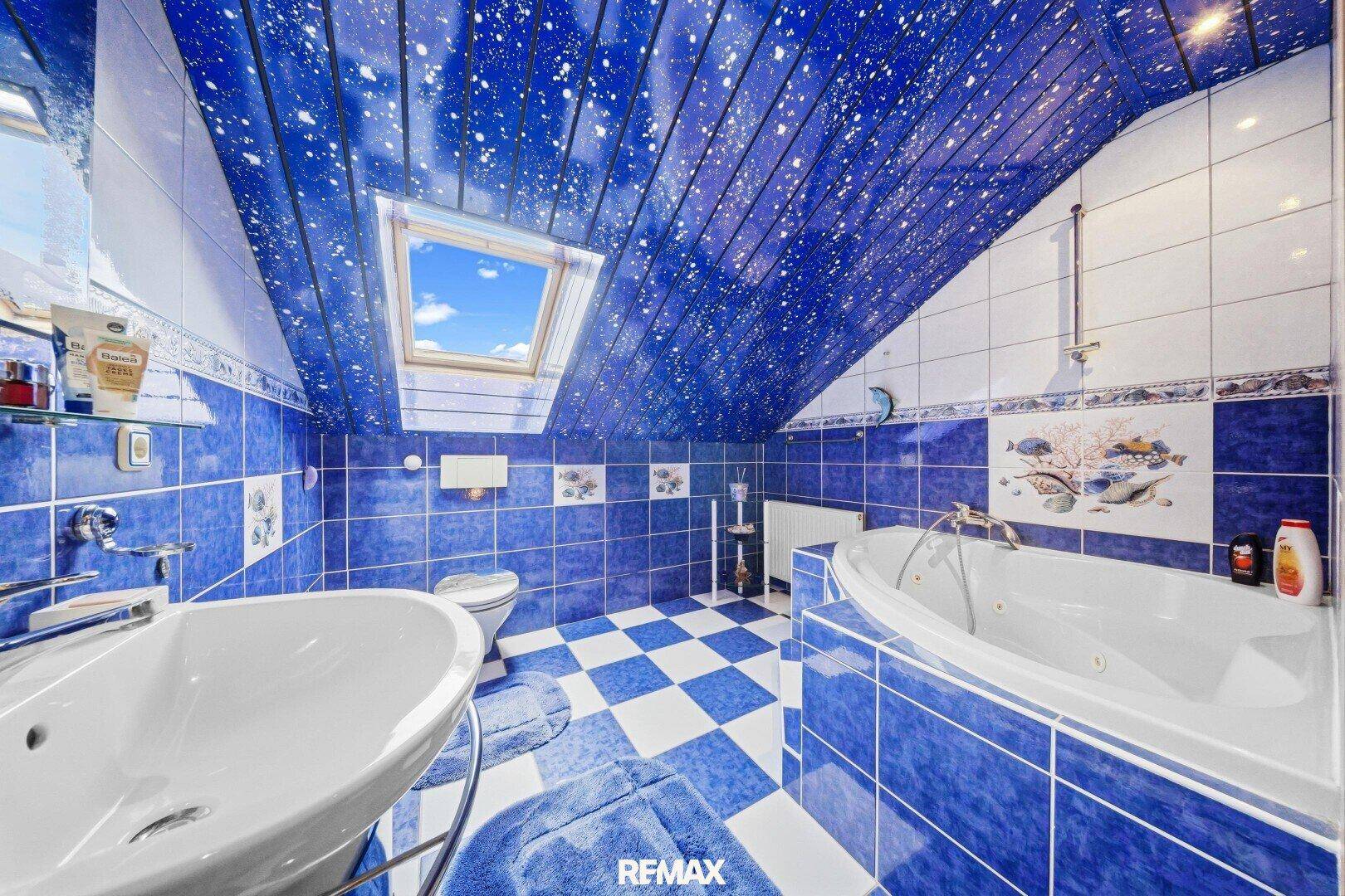Auffälliges Badezimmer im Dachgeschoss mit blauen Fliesen, Whirlpool und Dachfenster.