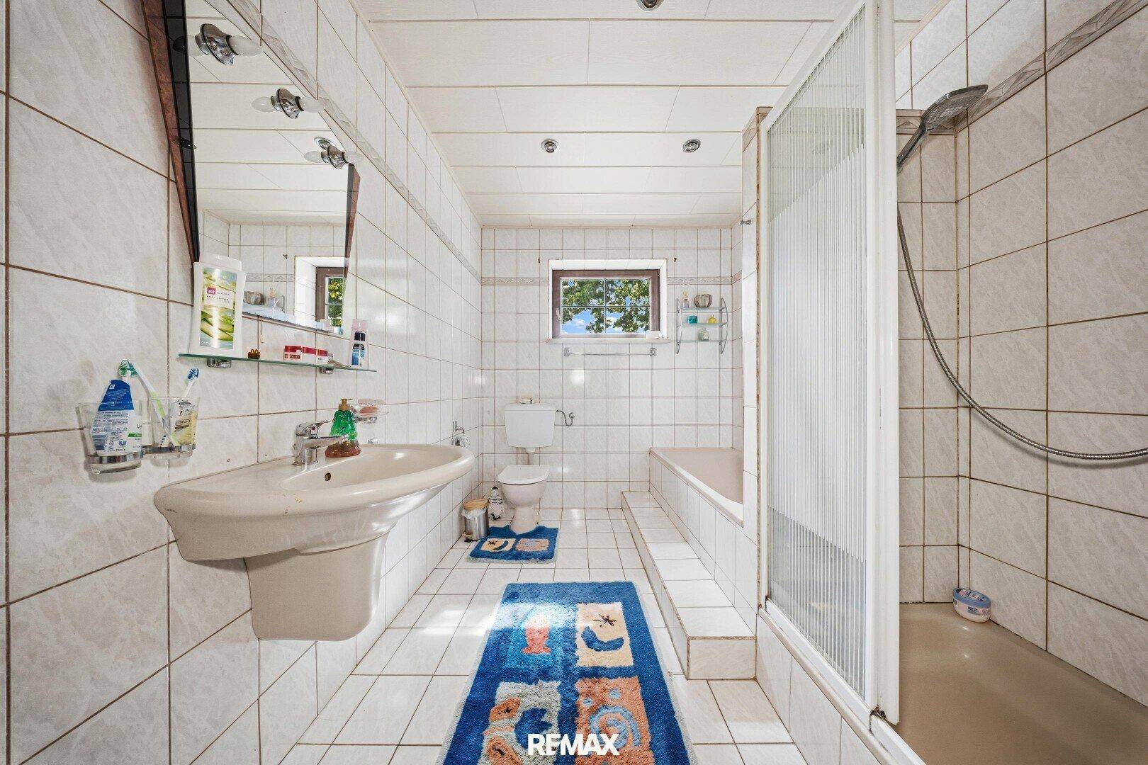 Gefliestes Badezimmer mit Badewanne, Dusche und Fenster, in hellem Design.