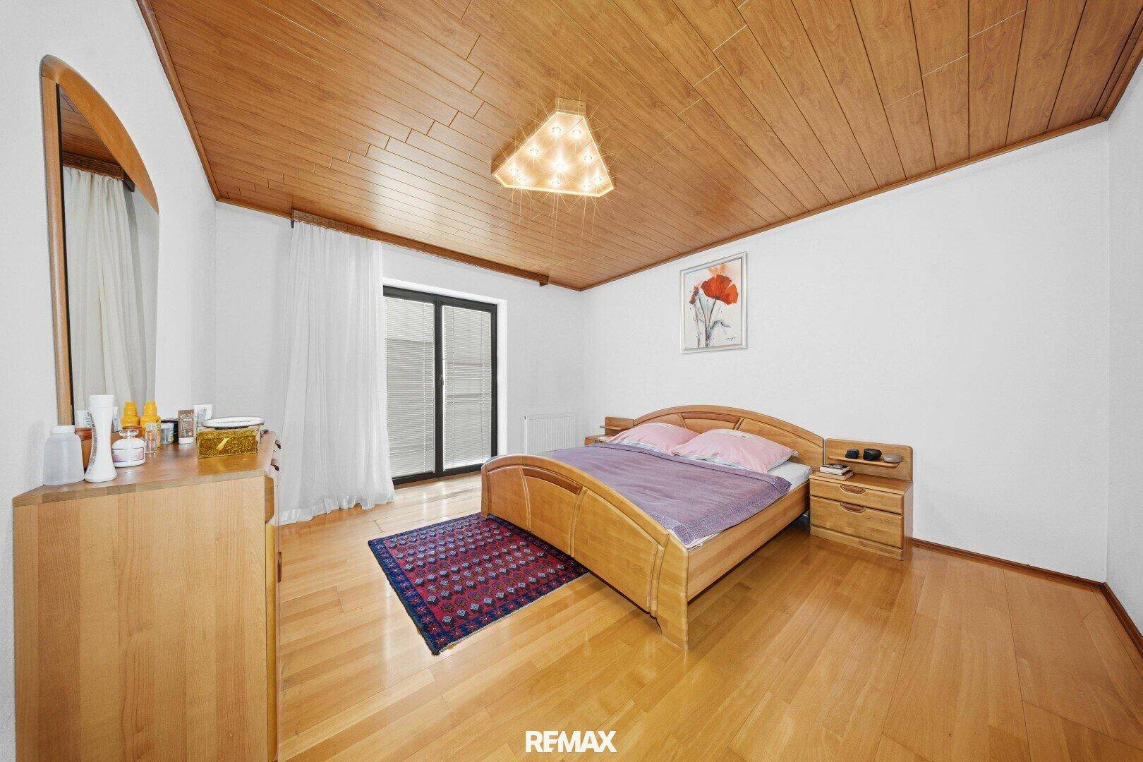 Schlafzimmer mit Holzdecke, Holzbett und Zugang zum Balkon.
