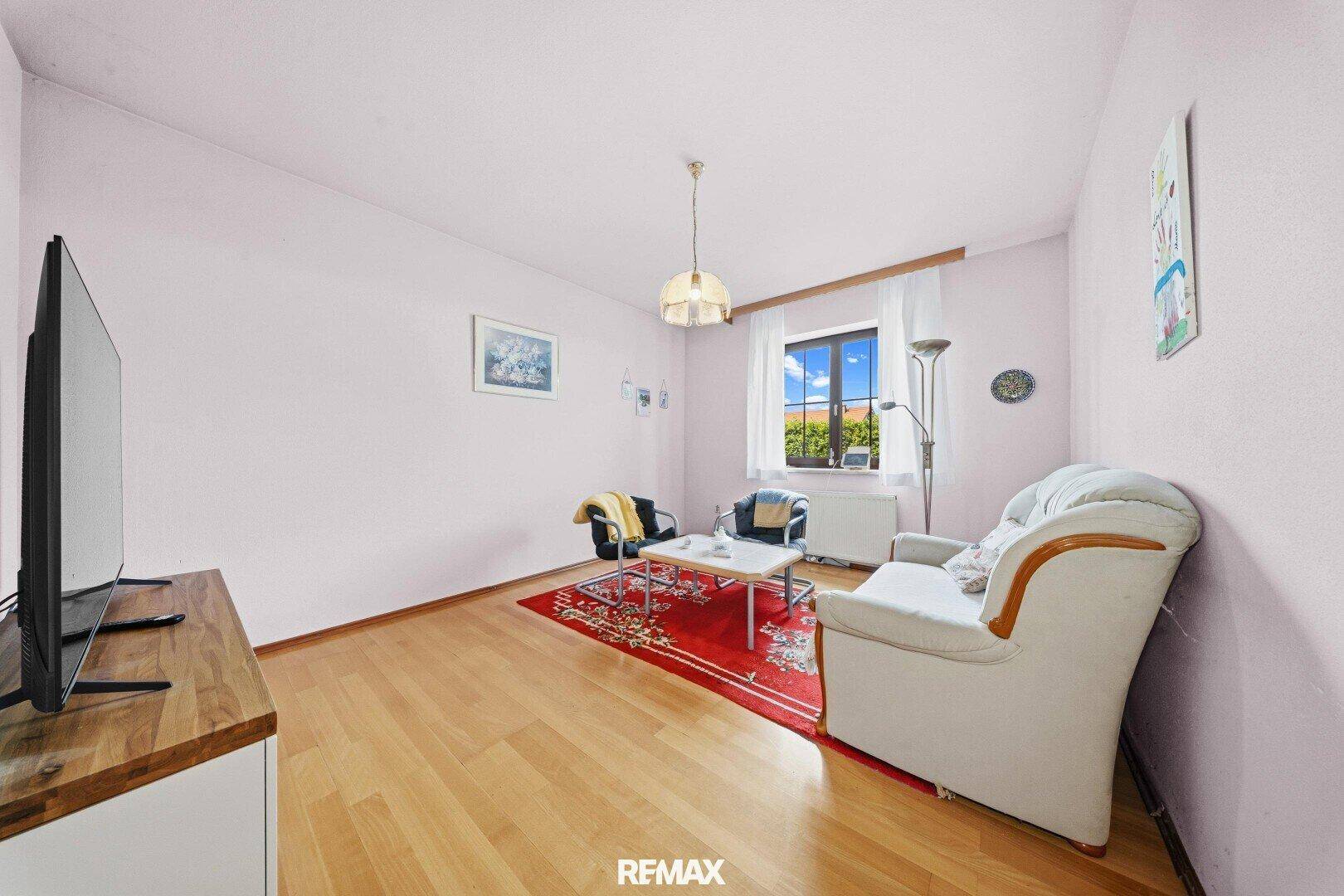 Helles Zimmer mit Holzboden, Sofa und Fernseher, vielseitig nutzbar.