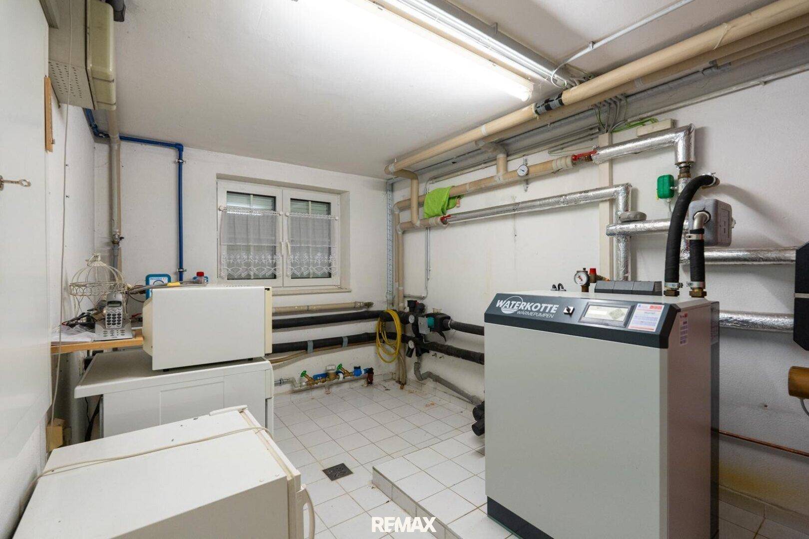 Heizungsraum mit technischer Ausstattung, Rohren und einem Fenster für Belüftung.