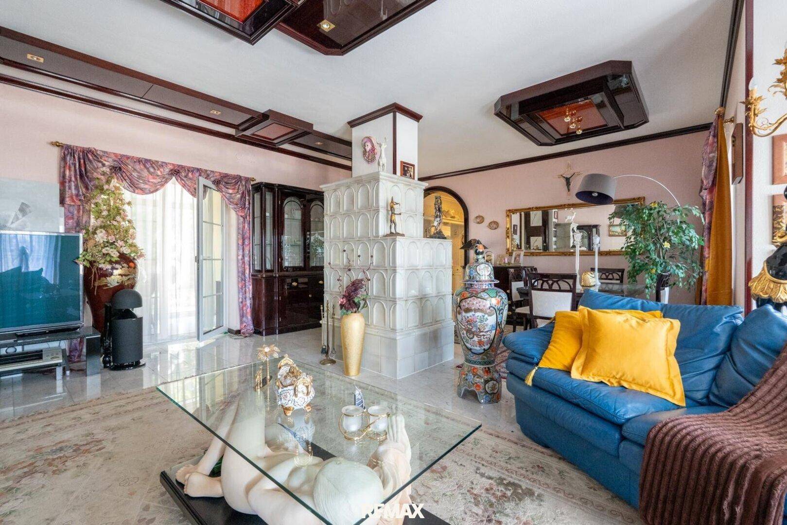 Gemütlicher Wohnbereich mit blauem Sofa, Kachelofen und Zugang zu einem Balkon oder Terrasse.