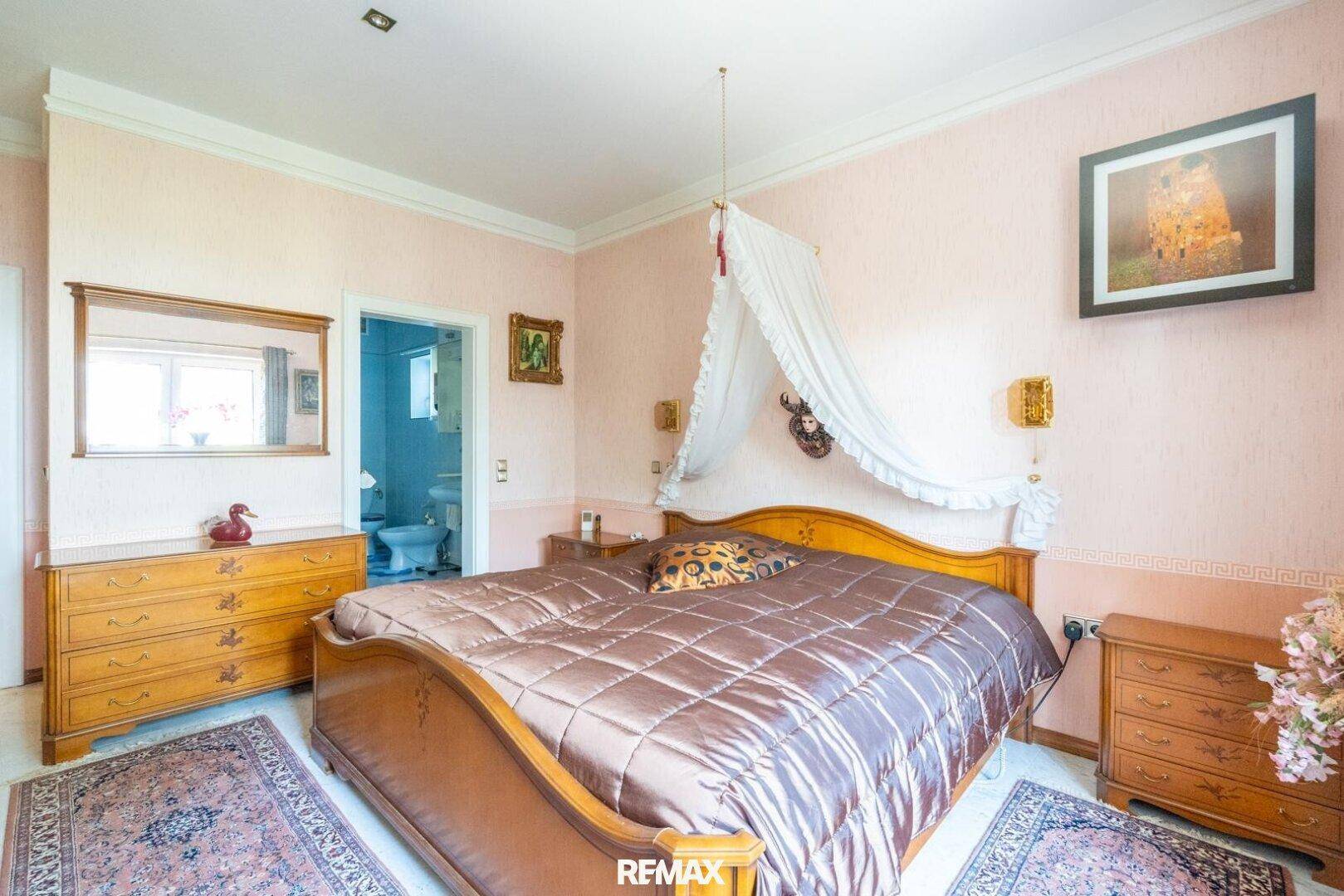 Schlafzimmer mit großem Bett, rosa Wänden und direktem Zugang zu einem Badezimmer.