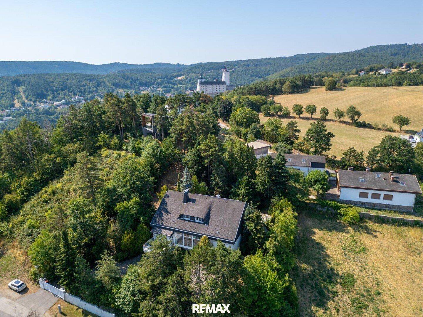 Panoramablick auf ein Haus in hügeliger Landschaft mit Wald und einem Schloss in der Ferne.