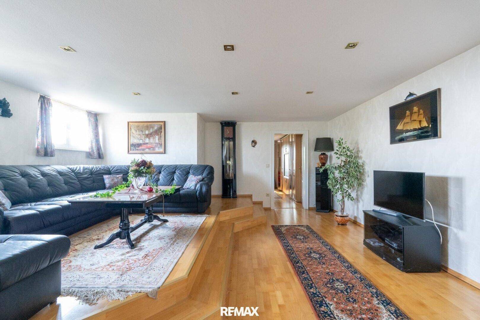 Geräumiges Wohnzimmer mit Ledersofa, Holzboden und einem erhöhten Bereich.