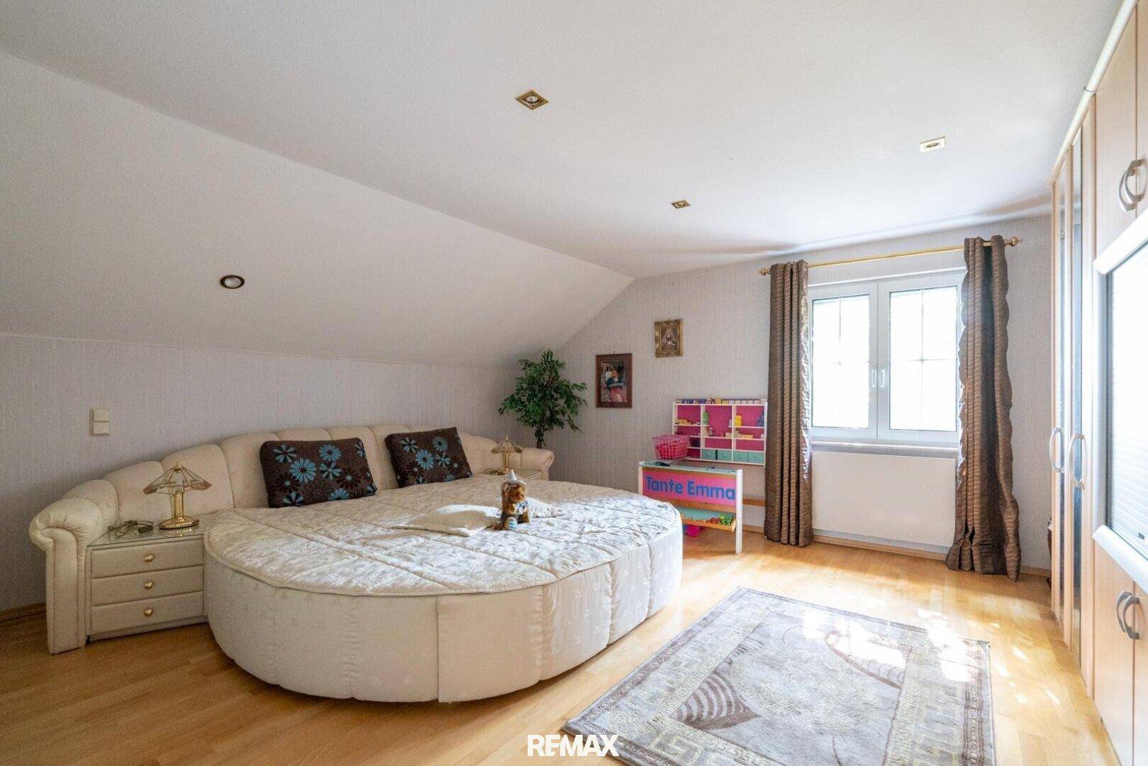Schlafzimmer im Dachgeschoss mit rundem Bett, Holzboden und Einbauschränken.
