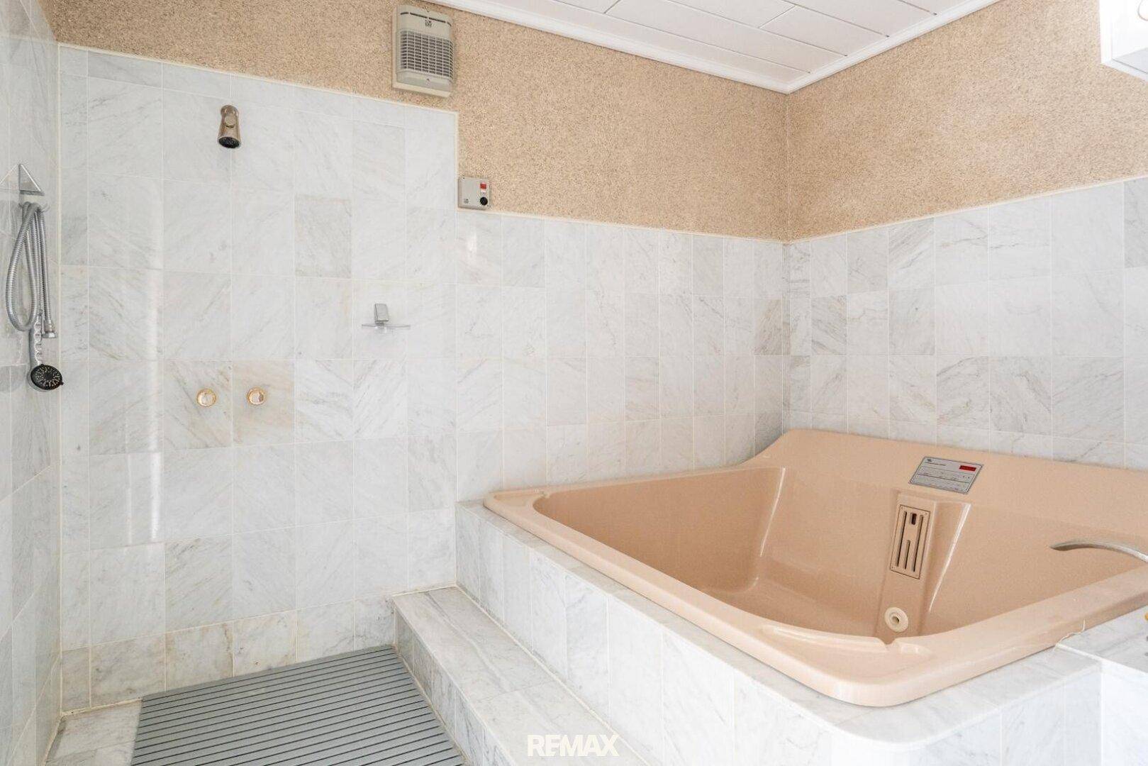 Badezimmer mit beiger Badewanne, Dusche und weißen Marmorfliesen an den Wänden.