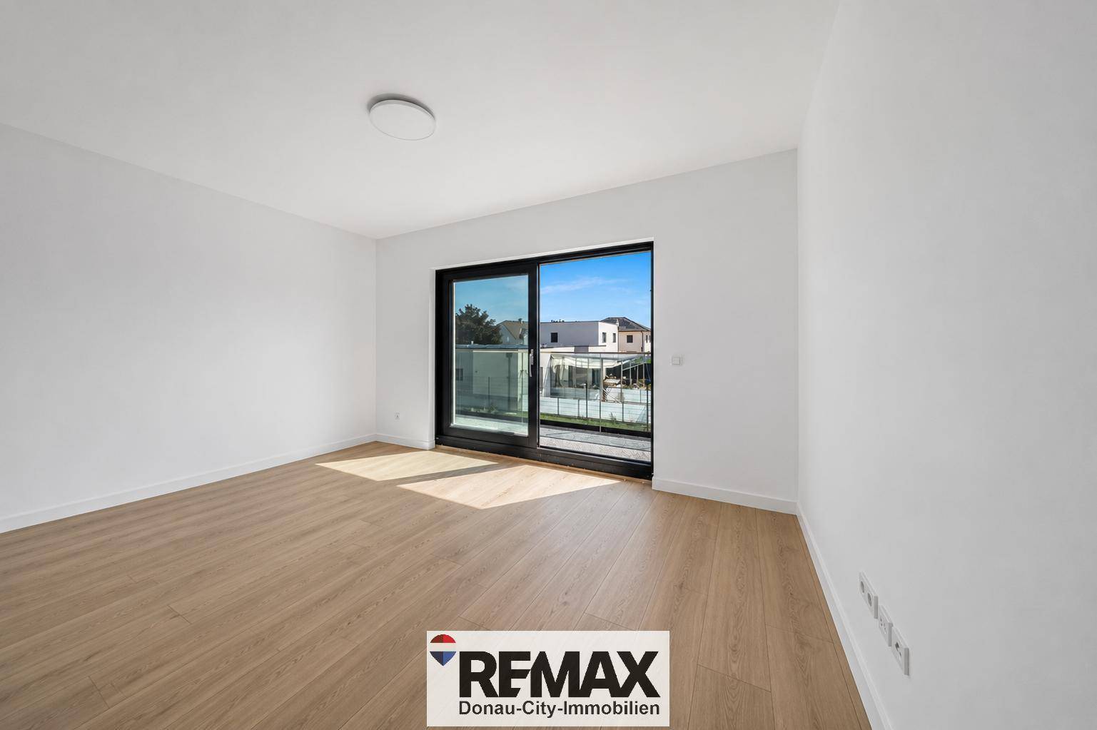 Leeres Schlafzimmer mit Holzboden und großem Fenster mit Zugang zum Balkon.
