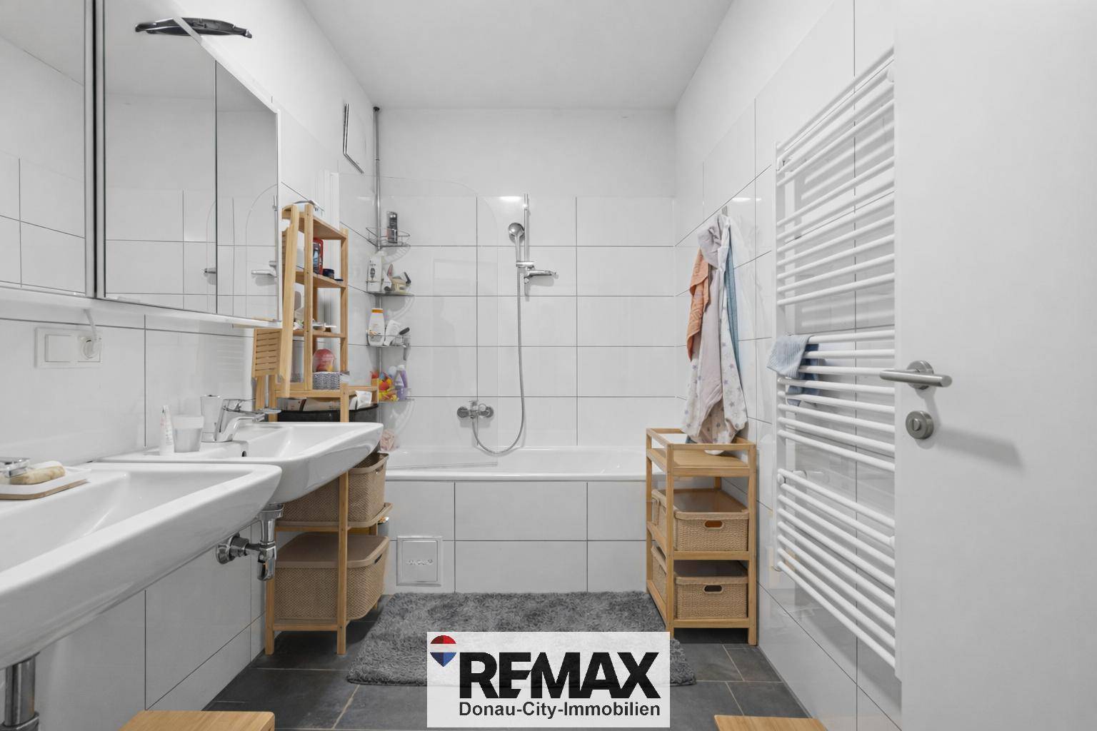 Helles Badezimmer mit Badewanne, Doppelwaschbecken und Handtuchheizkörper.