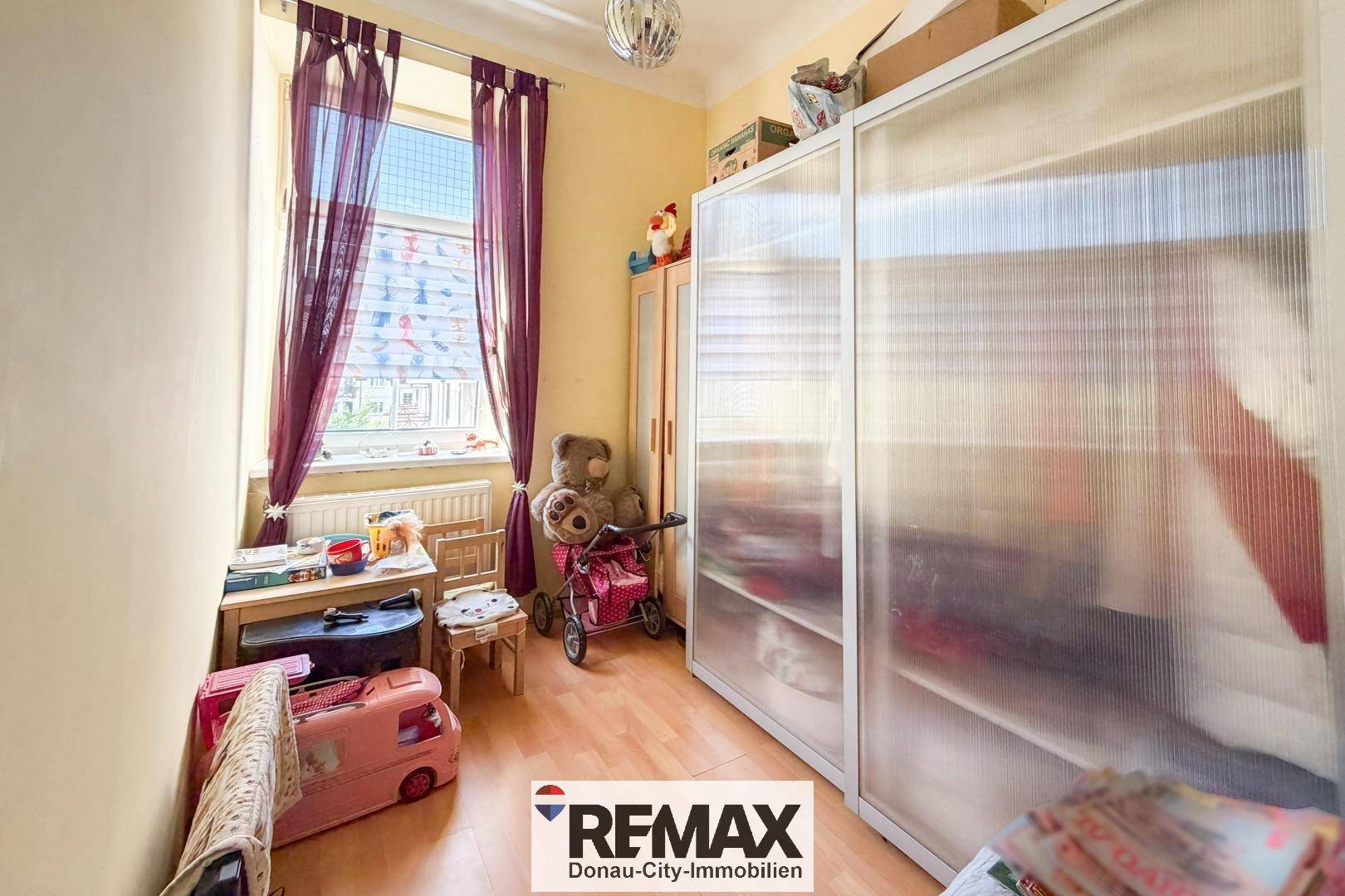 Kinderzimmer mit Spielzeug, einem Bett und einem großen, lichtdurchlässigen Kleiderschrank.