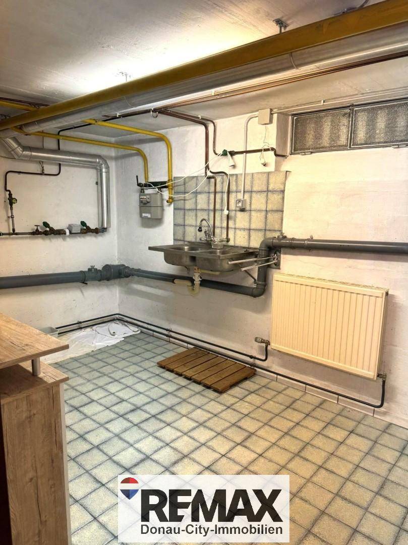 Hauswirtschaftsraum im Keller mit sichtbaren Rohren, Waschbecken und Fliesenboden.