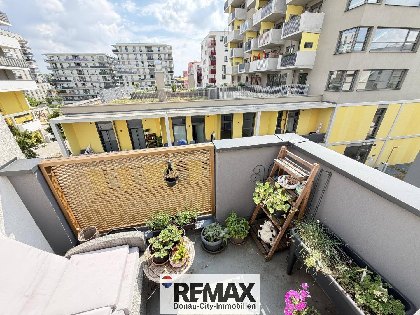 Kleiner, begrünter Balkon mit Sitzgelegenheiten und Blick auf die umliegenden Gebäude.