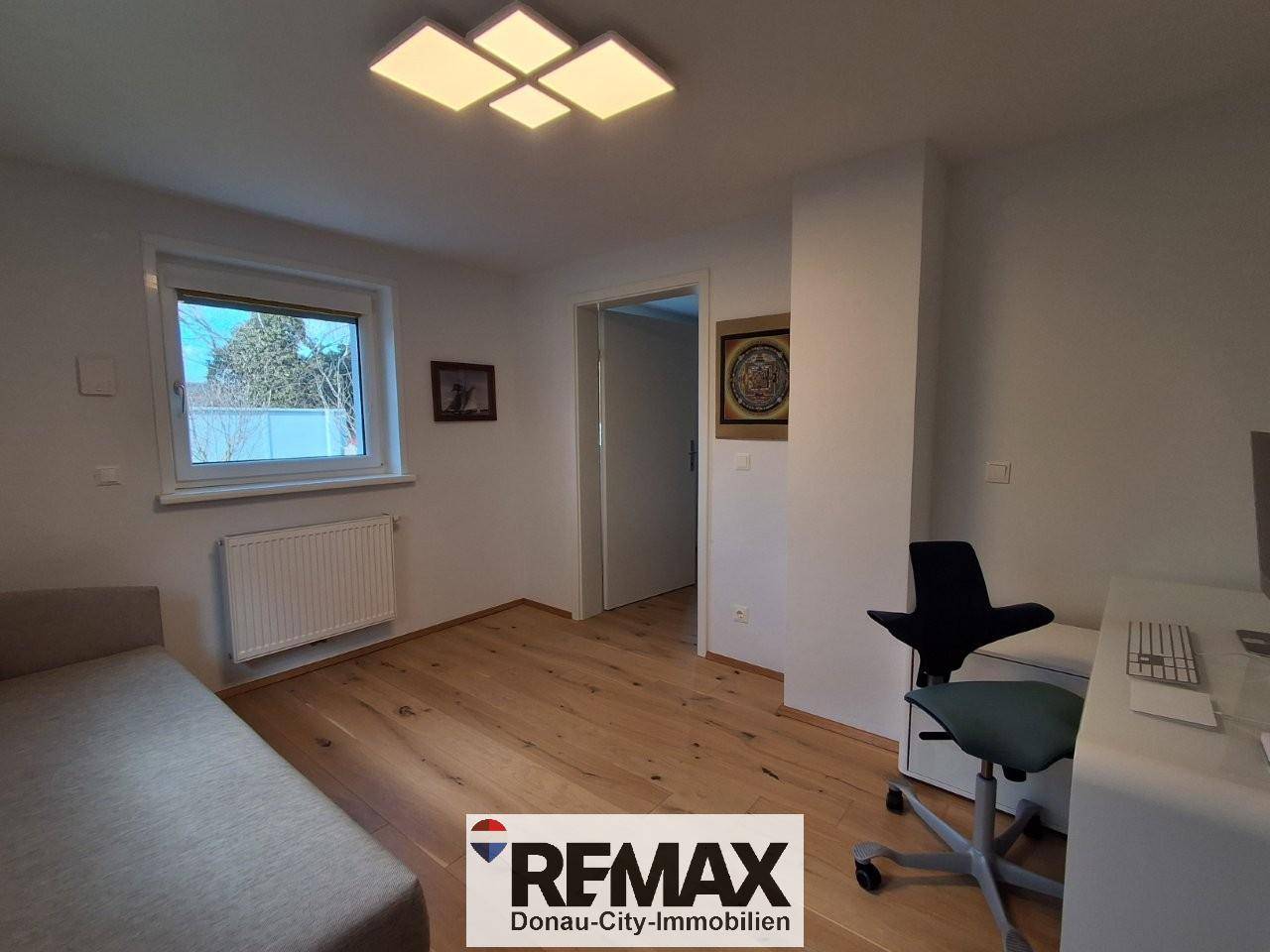 Helles Arbeitszimmer mit Holzfußboden, Fenster und modernem Deckenlicht.
