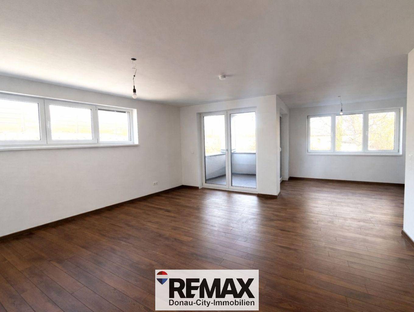 Geräumiges Wohnzimmer mit Holzboden und großen Fenstern, die viel Licht hereinlassen.