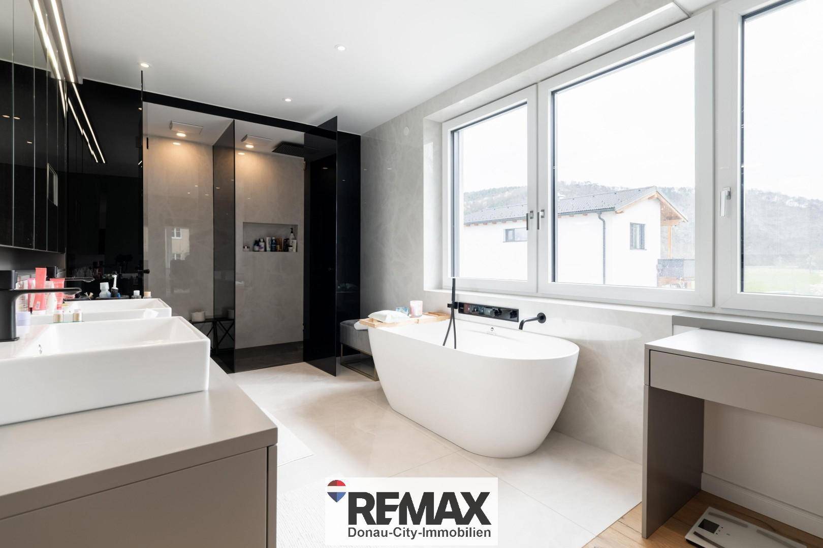 Luxuriöses Badezimmer mit freistehender Badewanne, Doppelwaschbecken und großer Fensterfront.