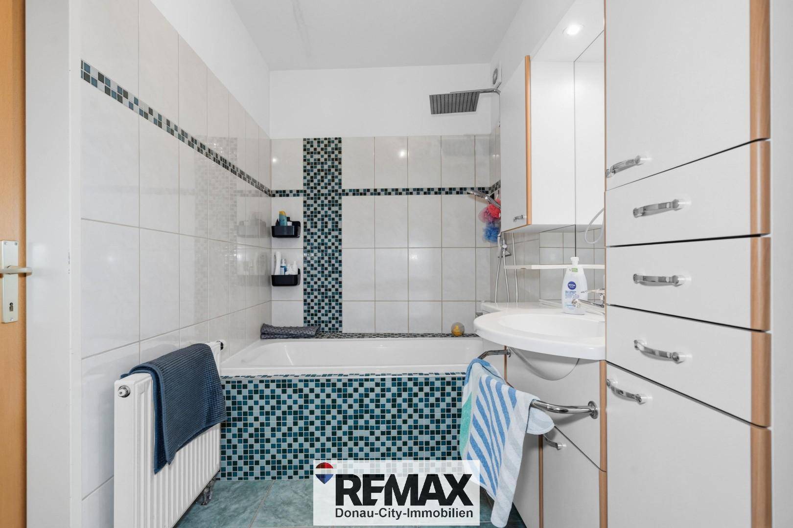 Badezimmer mit Badewanne, Dusche und weißen Fliesen mit blauen Akzenten.