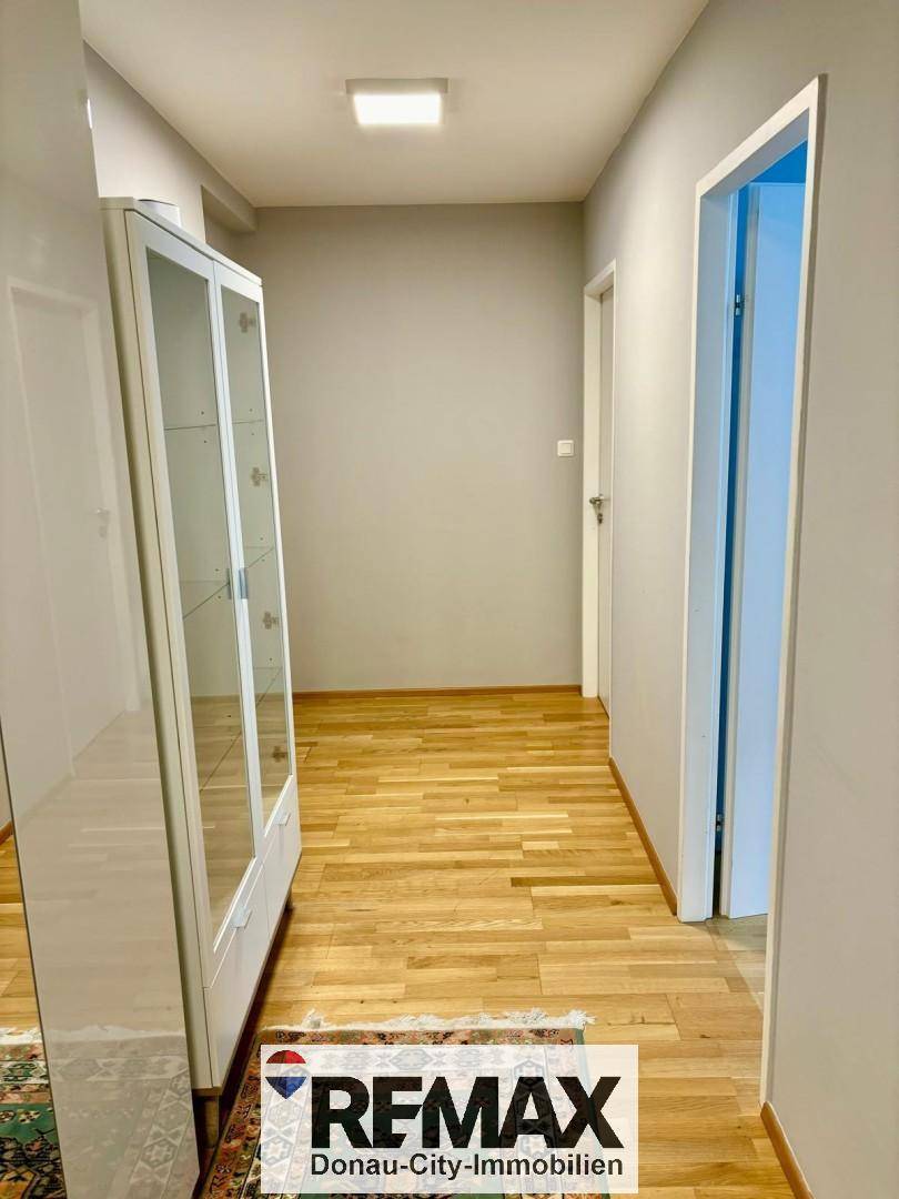 Heller Flur mit Holzboden und einem weißen Vitrinenschrank.