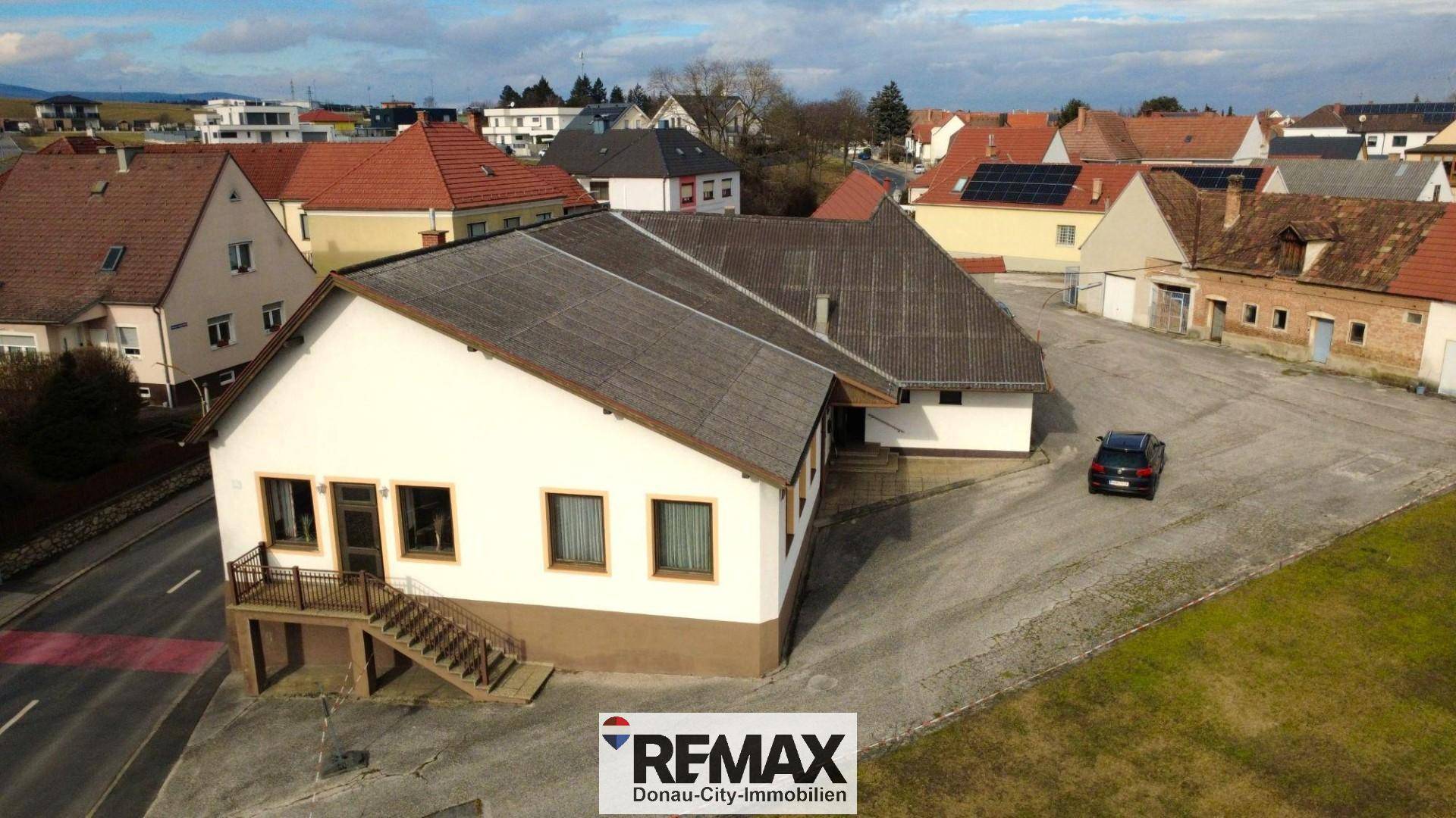 Gebäudekomplex aus erhöhter Perspektive mit Zufahrt, Parkplätzen und umliegender Bebauung.