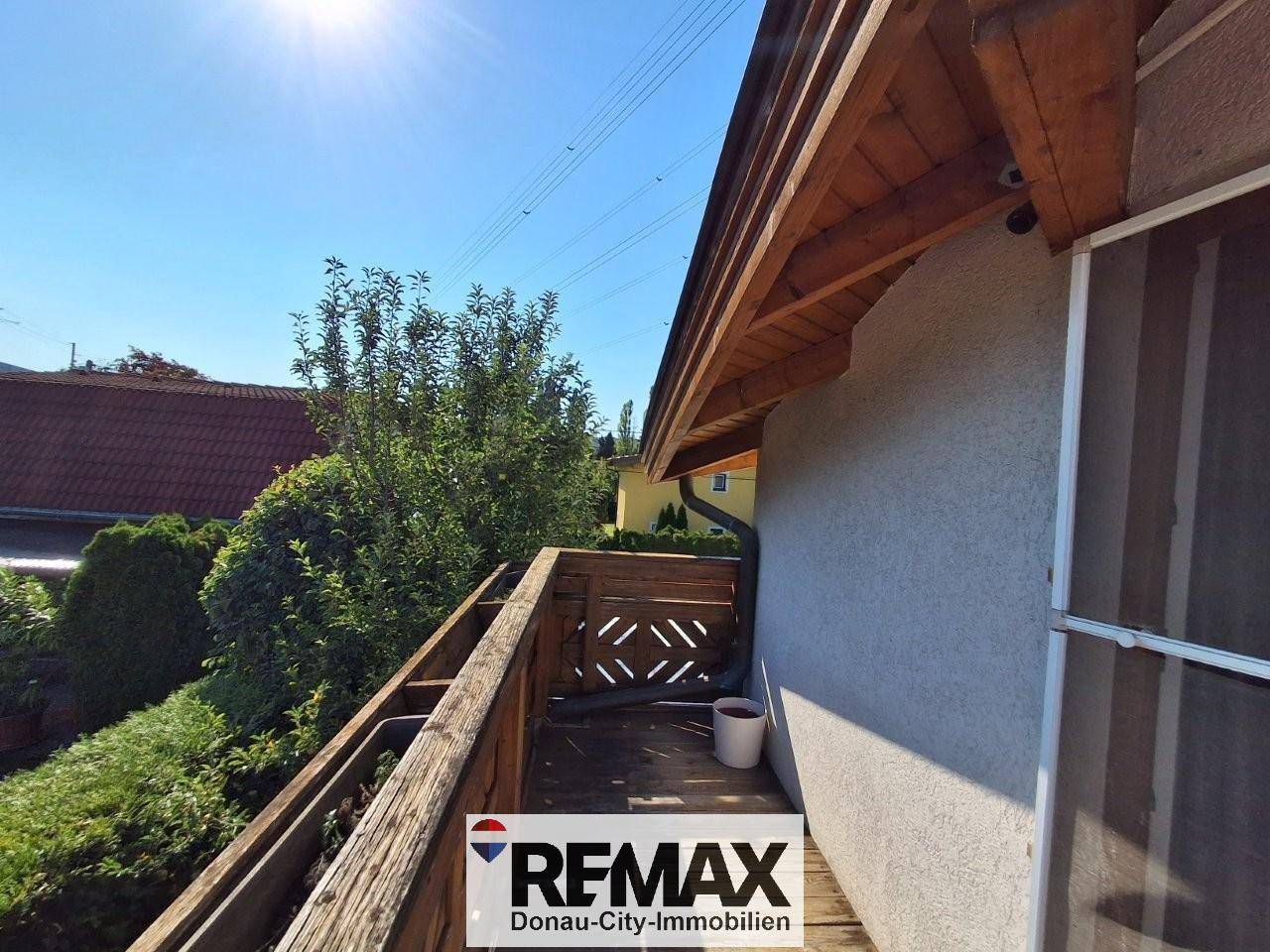 Sonniger Balkon mit Holzgeländer und Blick auf die grüne Umgebung und benachbarte Häuser.