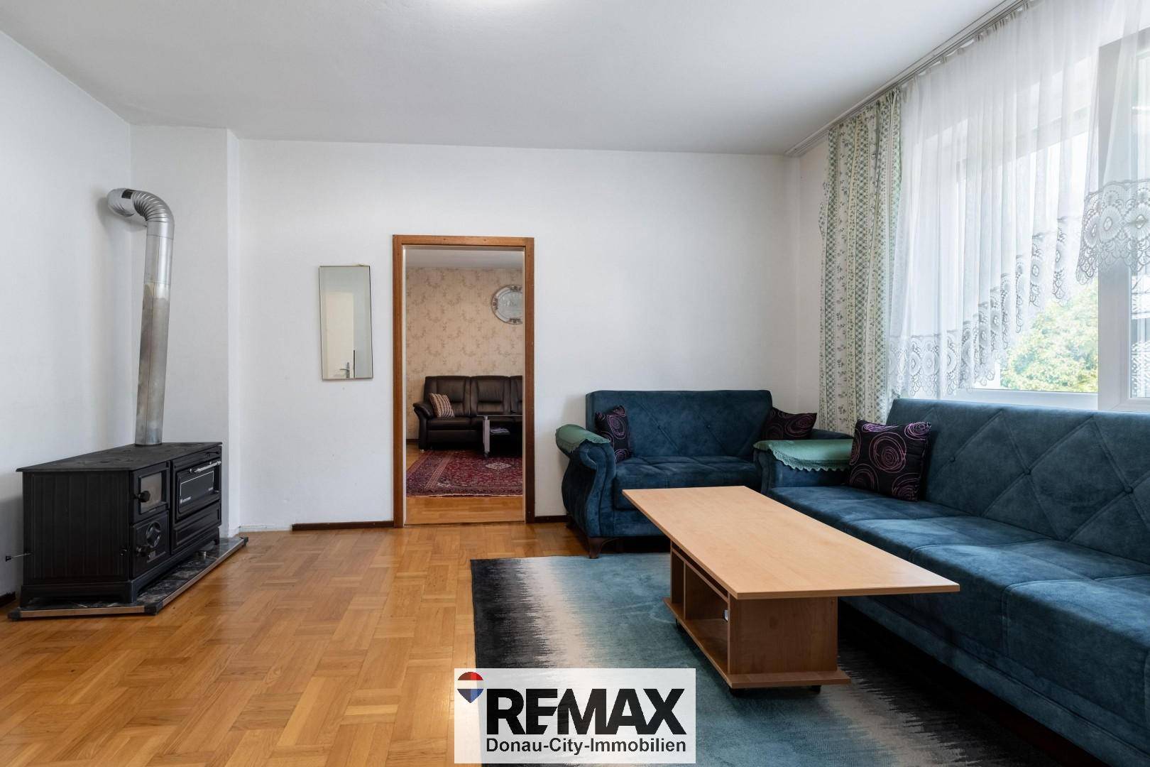 Wohnzimmer mit Holzofen, blauen Sofas und Blick in einen weiteren Raum.