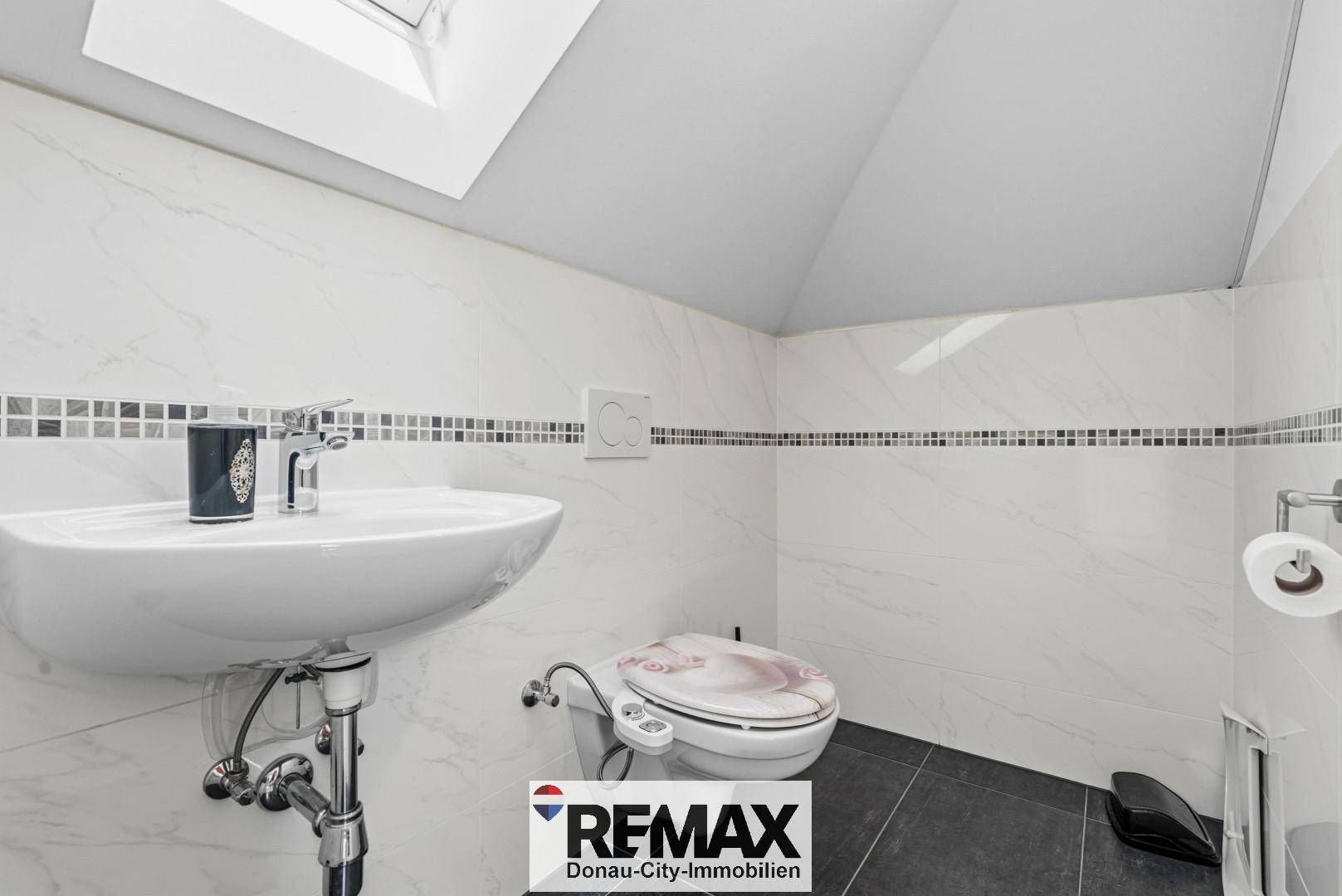 Kleines WC im Dachgeschoss mit Waschbecken, Toilette und Dachfenster.