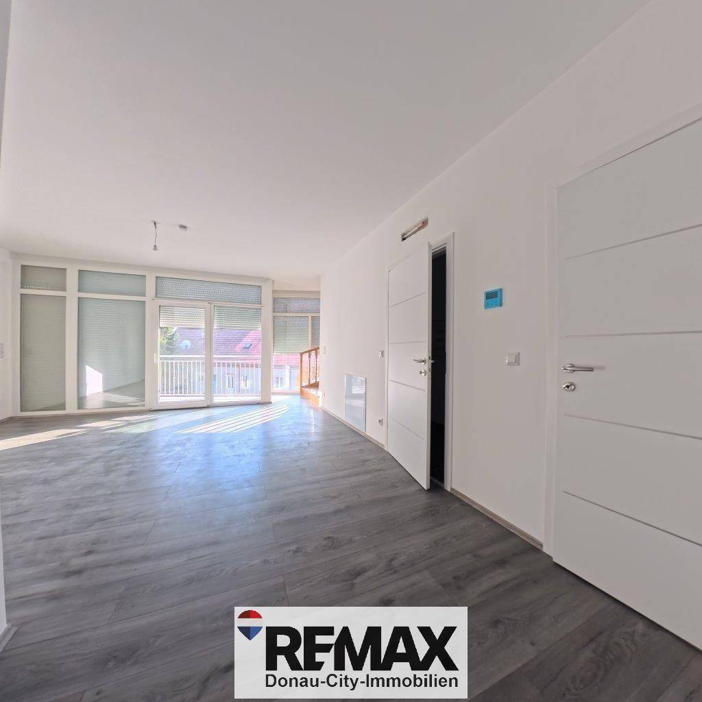 Lichtdurchfluteter Wohnbereich mit großen Fenstern, Laminatboden und Zugang zu einem Balkon.