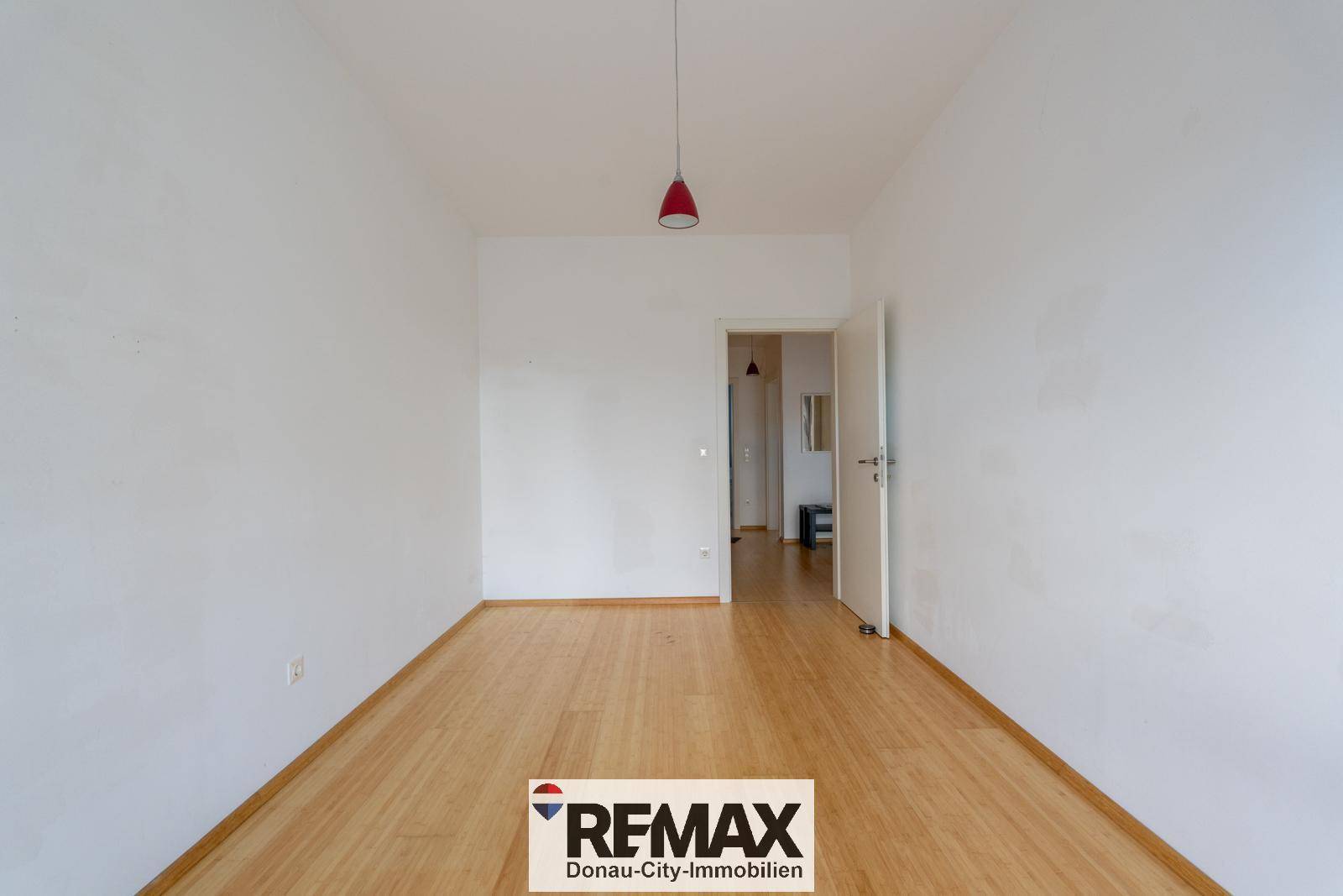 Leeres Zimmer mit Holzfußboden und offener Tür zu einem angrenzenden Bereich.