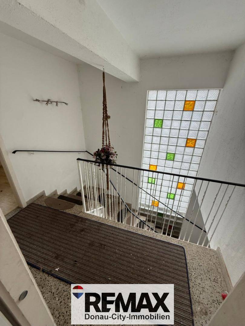 Treppenaufgang mit Terrazzoboden und einem dekorativen Glasbausteinfenster, das den Raum erhellt.