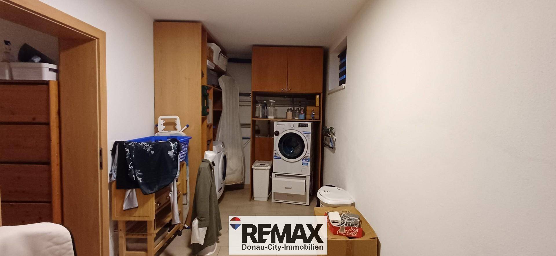 Waschküche mit Waschmaschine, Trockner und Regalen für Wäsche.