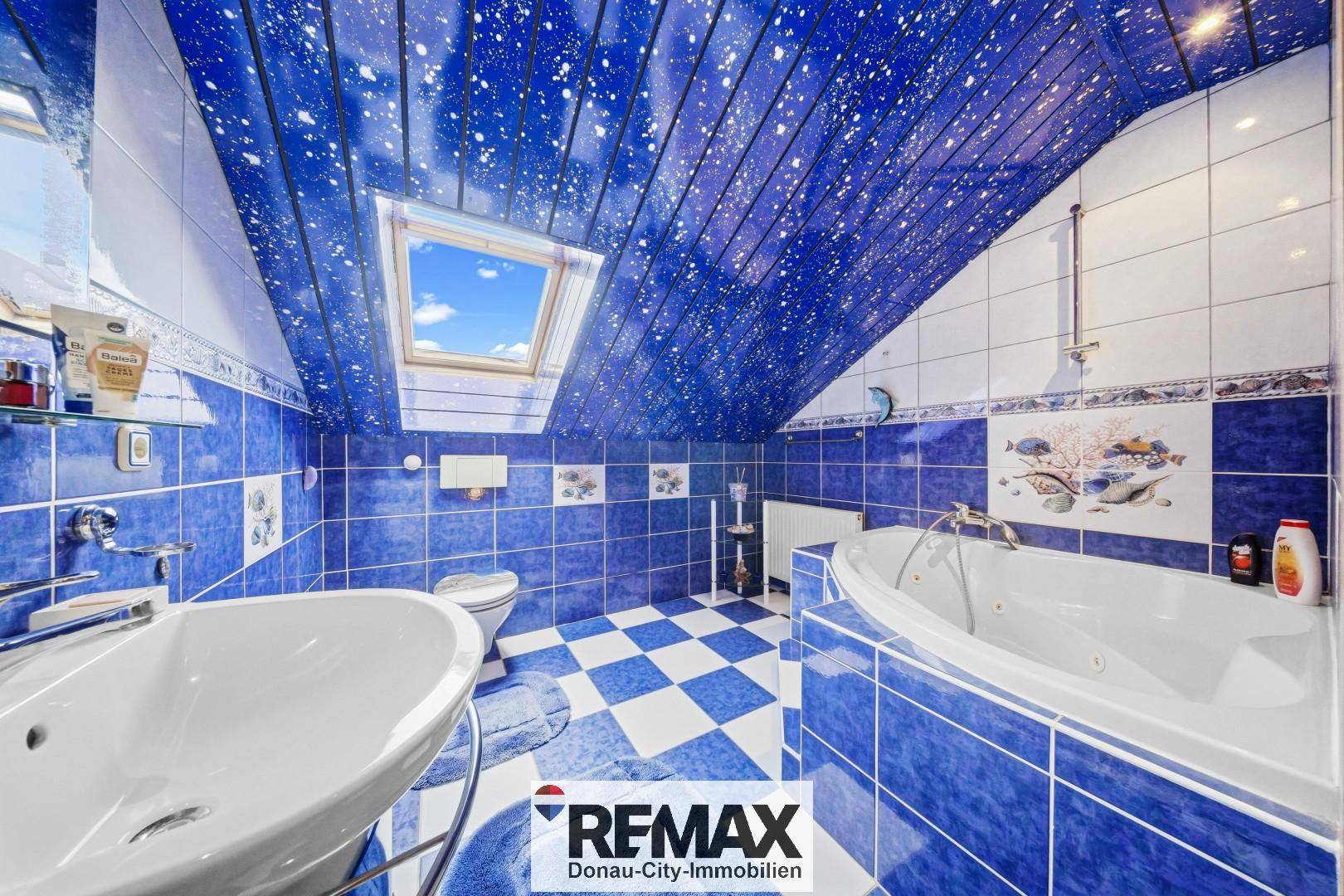 Auffälliges Badezimmer im Dachgeschoss mit blauen Fliesen, Whirlpool-Badewanne und Dachfenster.