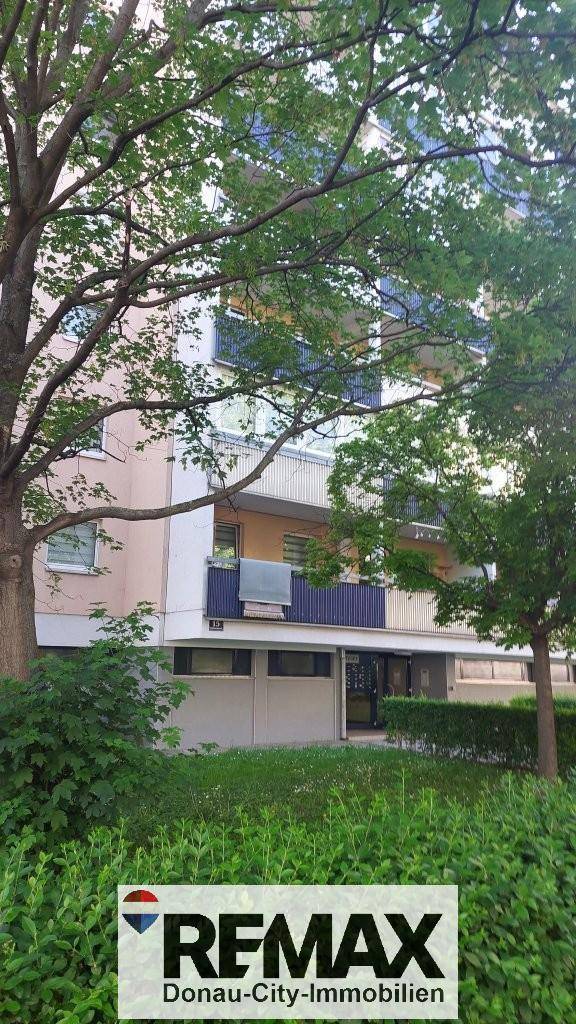Mehrfamilienhaus mit grüner Umgebung, Balkonen und großen Fenstern.