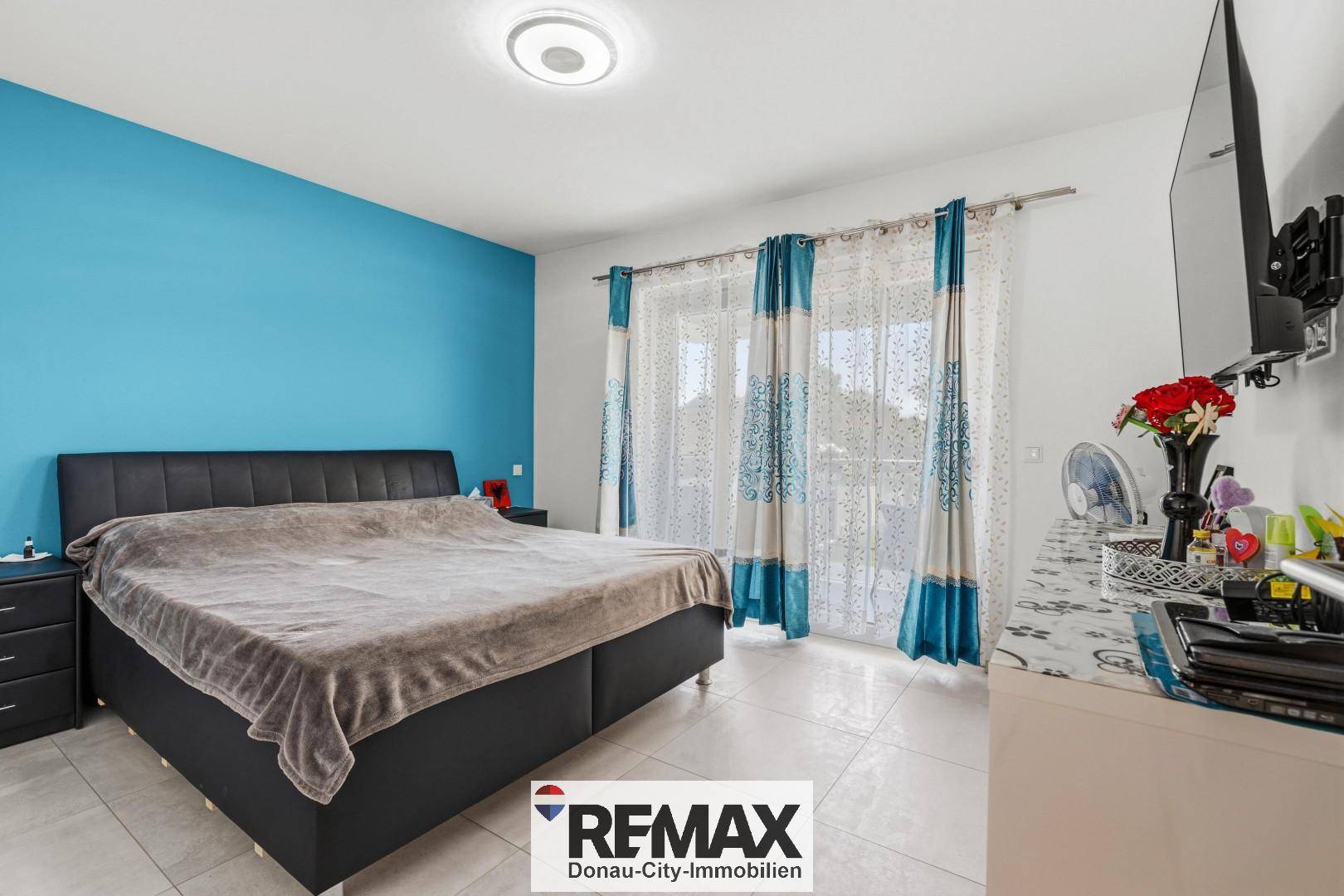 Schlafzimmer mit blau akzentuierter Wand, großem Bett und Zugang zum Balkon.