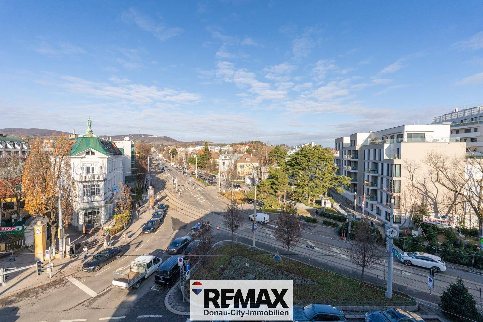 Weitläufiger Blick über die Stadt mit Straßen, Gebäuden und bewaldeten Hügeln im Hintergrund.
