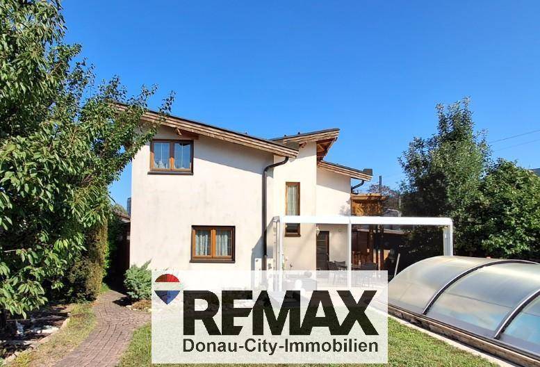 Ansicht des Hauses vom Garten aus mit heller Fassade, Fenstern und dem überdachten Swimmingpool.