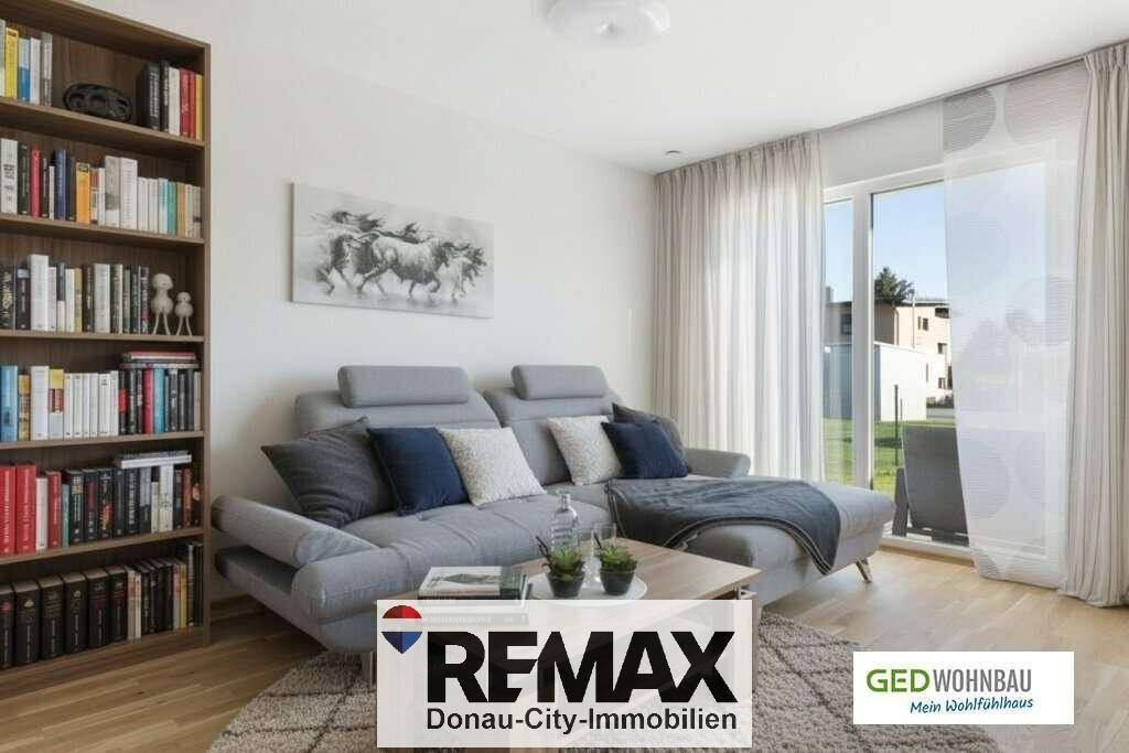 Gemütliches Wohnzimmer mit grauem Sofa, Bücherregal und Zugang zur sonnigen Terrasse.