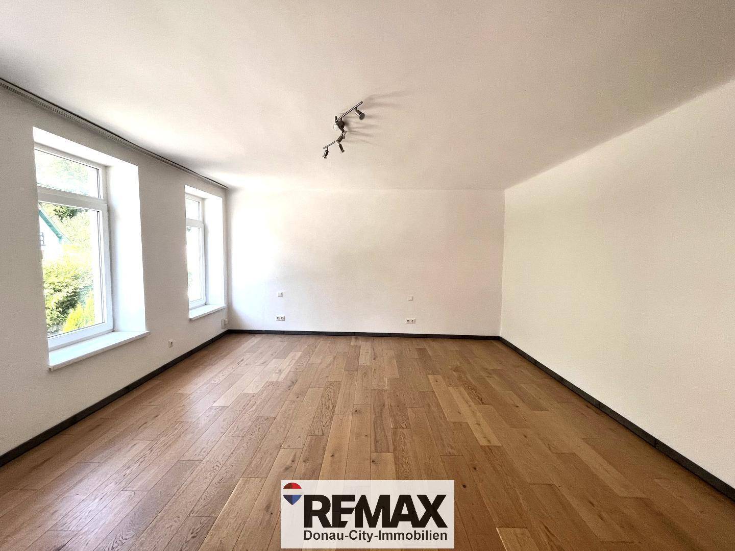 Lichtdurchfluteter Raum mit Holzboden und zwei großen Fenstern, bereit zur individuellen Gestaltung.