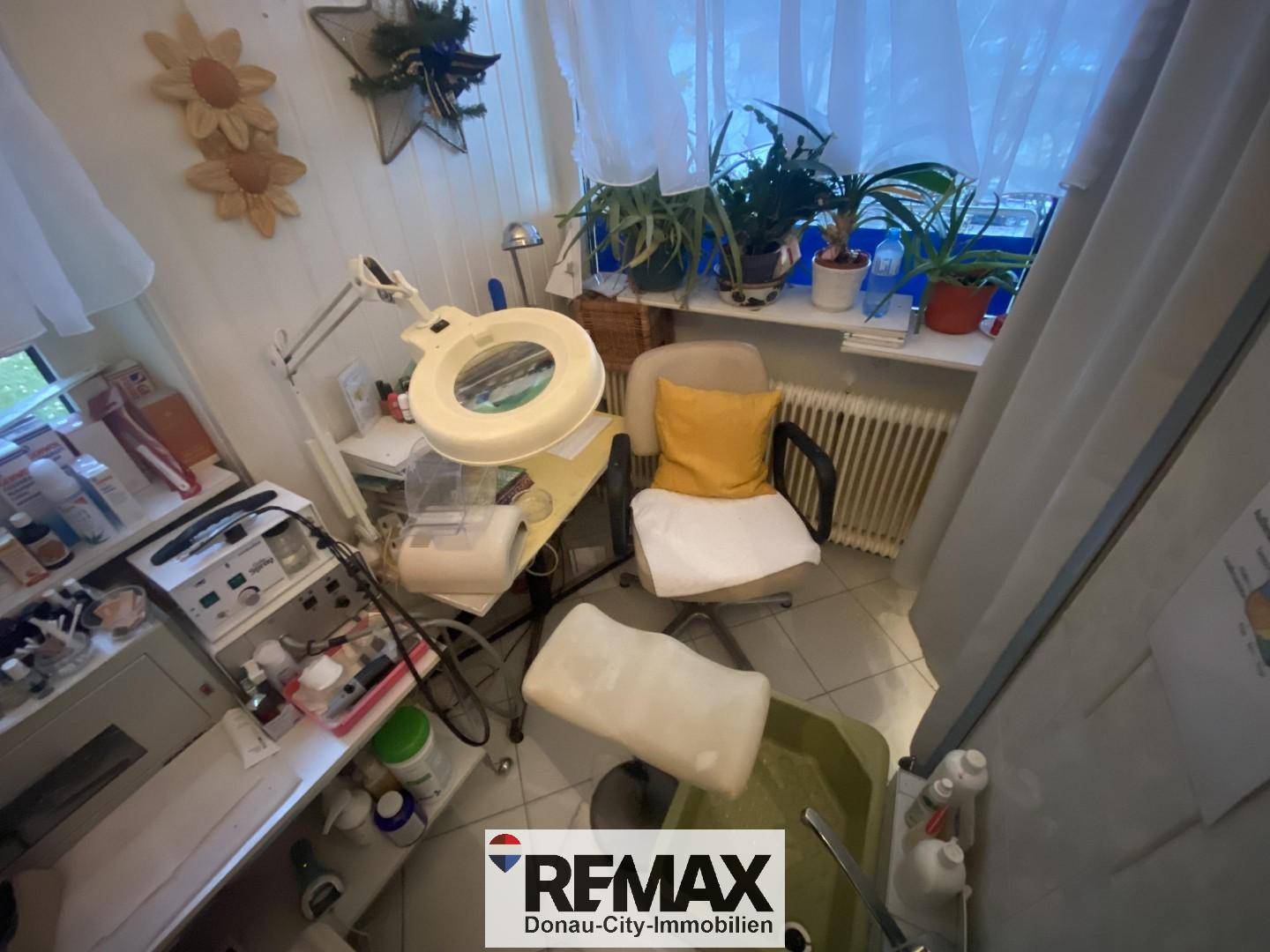 Behandlungsraum oder Büro mit Arbeitsplatz, Pflanzen und Heizkörper unter dem Fenster.