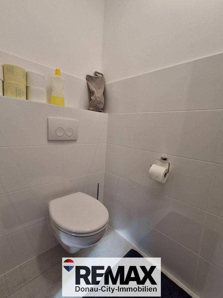 Kleines Gäste-WC mit wandhängender Toilette und weißen Fliesen an den Wänden.