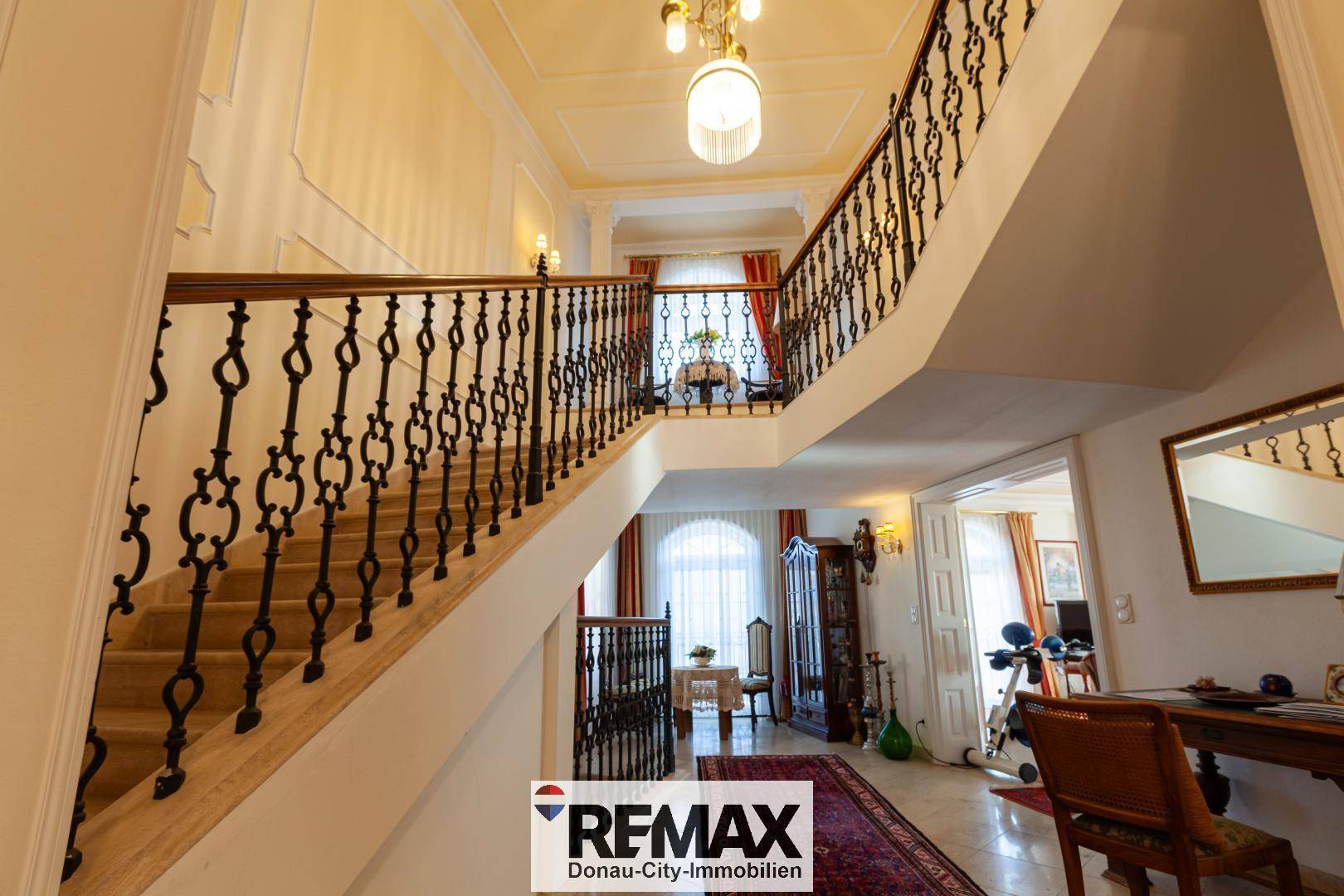 Elegantes Treppenhaus mit geschwungener Marmortreppe, schmiedeeisernem Geländer und hohen Decken.