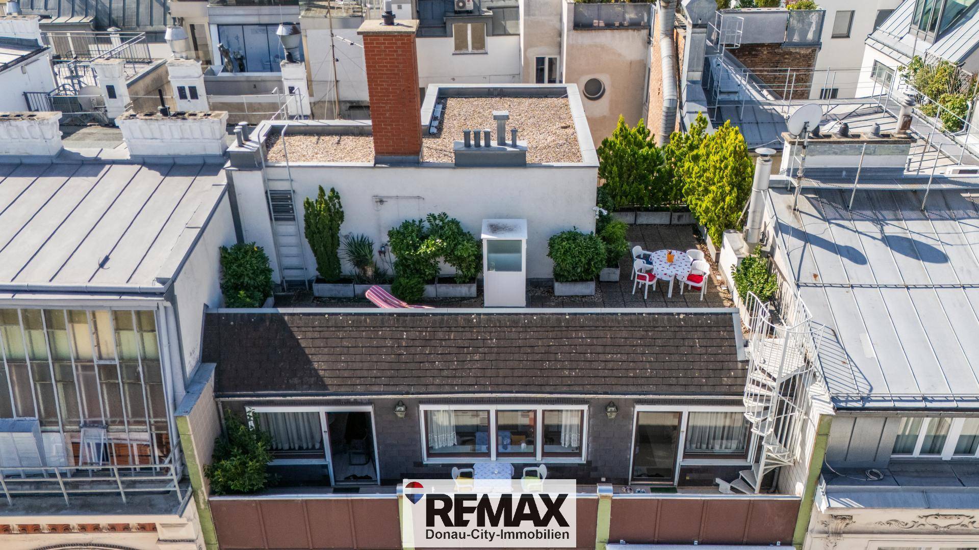 Luftaufnahme eines Gebäudes mit einer möblierten Dachterrasse und grünen Pflanzen.