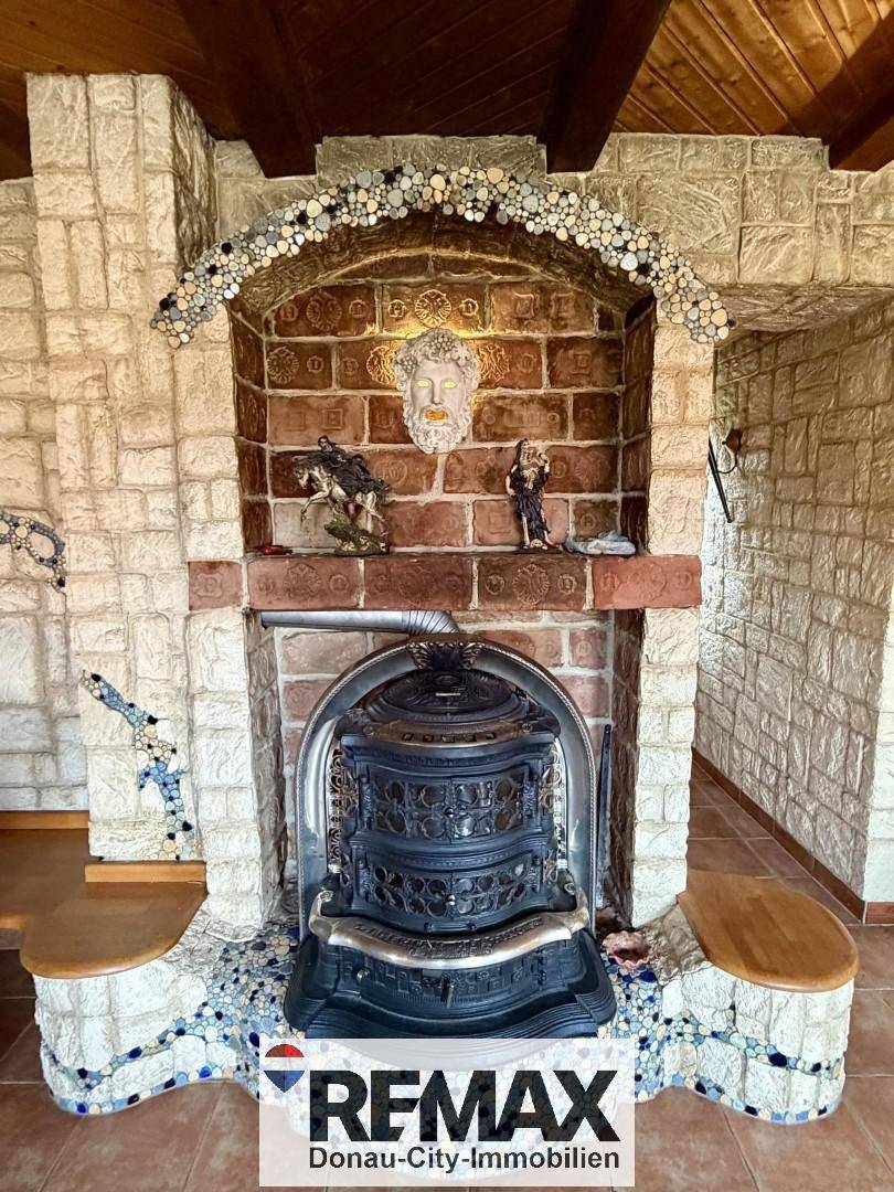 Detailansicht eines rustikalen Kamins mit gusseisernem Ofen, verziert mit Stein- und Mosaikelementen.