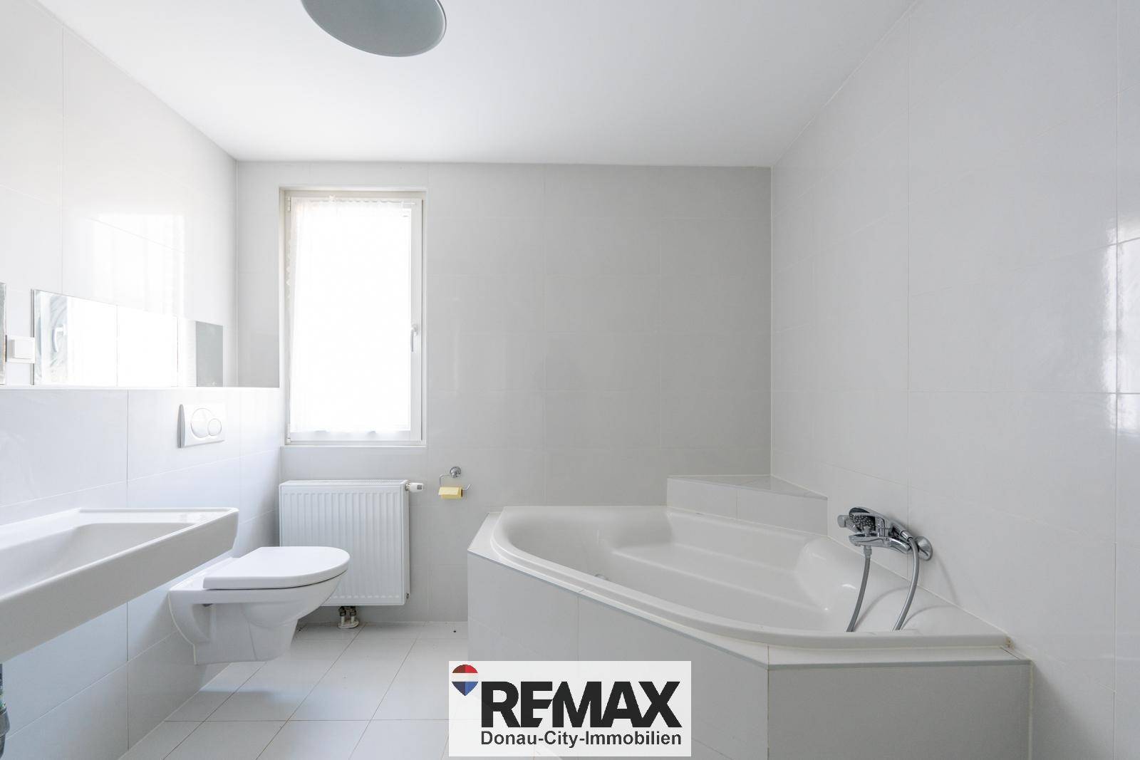 Helles Badezimmer mit Eckbadewanne, Waschbecken, Toilette und Fenster für natürliche Belüftung.