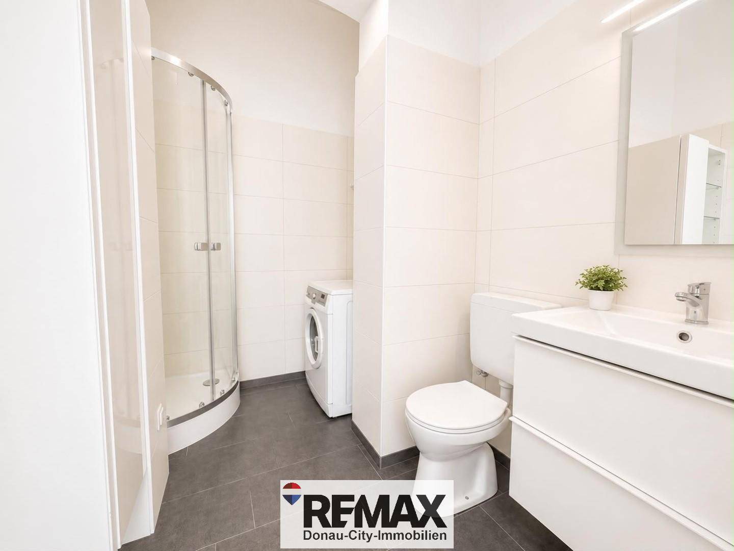 Modernes Badezimmer mit Dusche, Waschbecken, Toilette und Waschmaschine, hell gefliest.