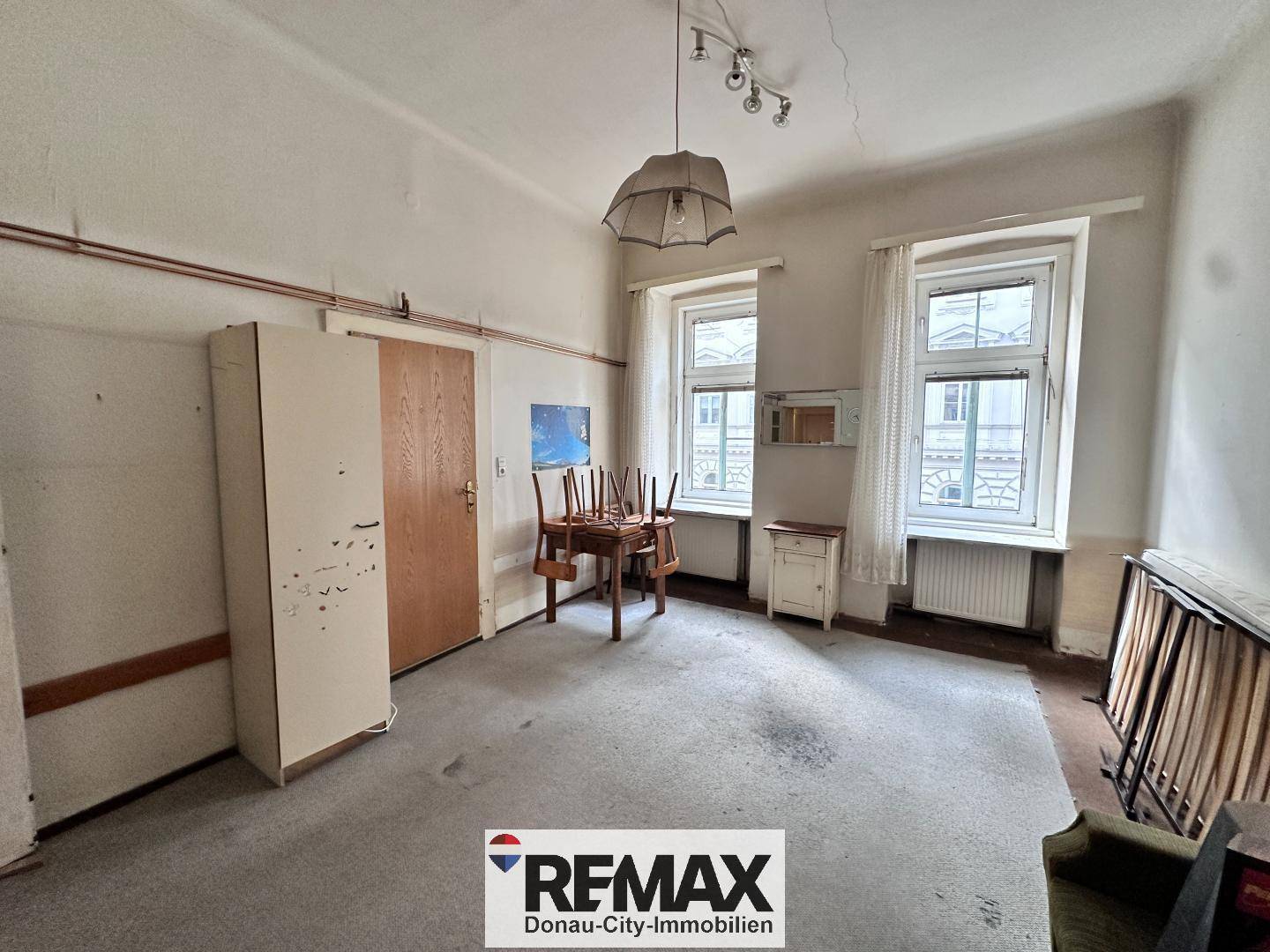 Geräumiges Zimmer mit Teppichboden, zwei Fenstern und einem Tisch mit Stühlen.