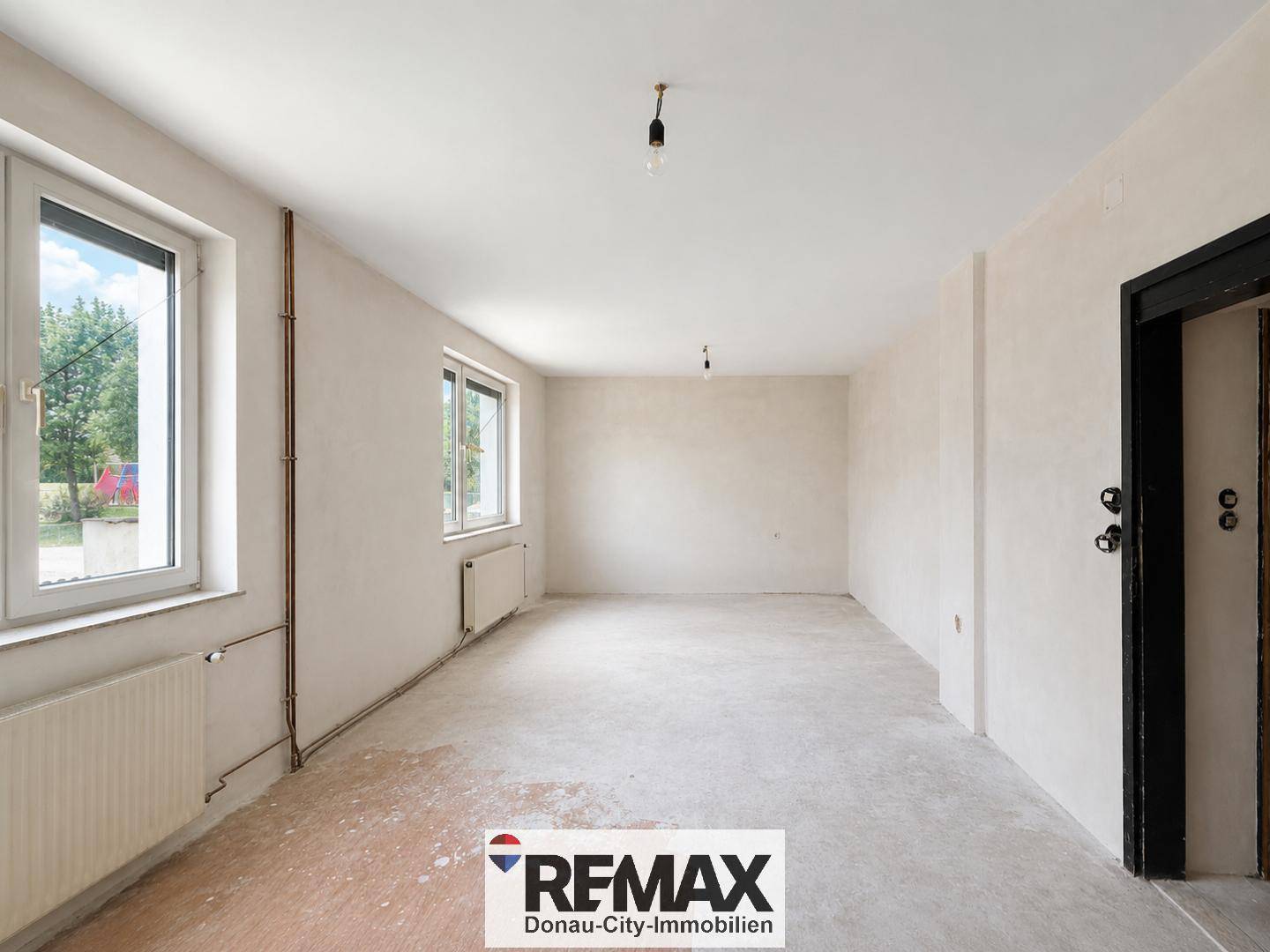 Geräumiger Raum in Renovierung mit zwei Fenstern und unfertigem Boden.